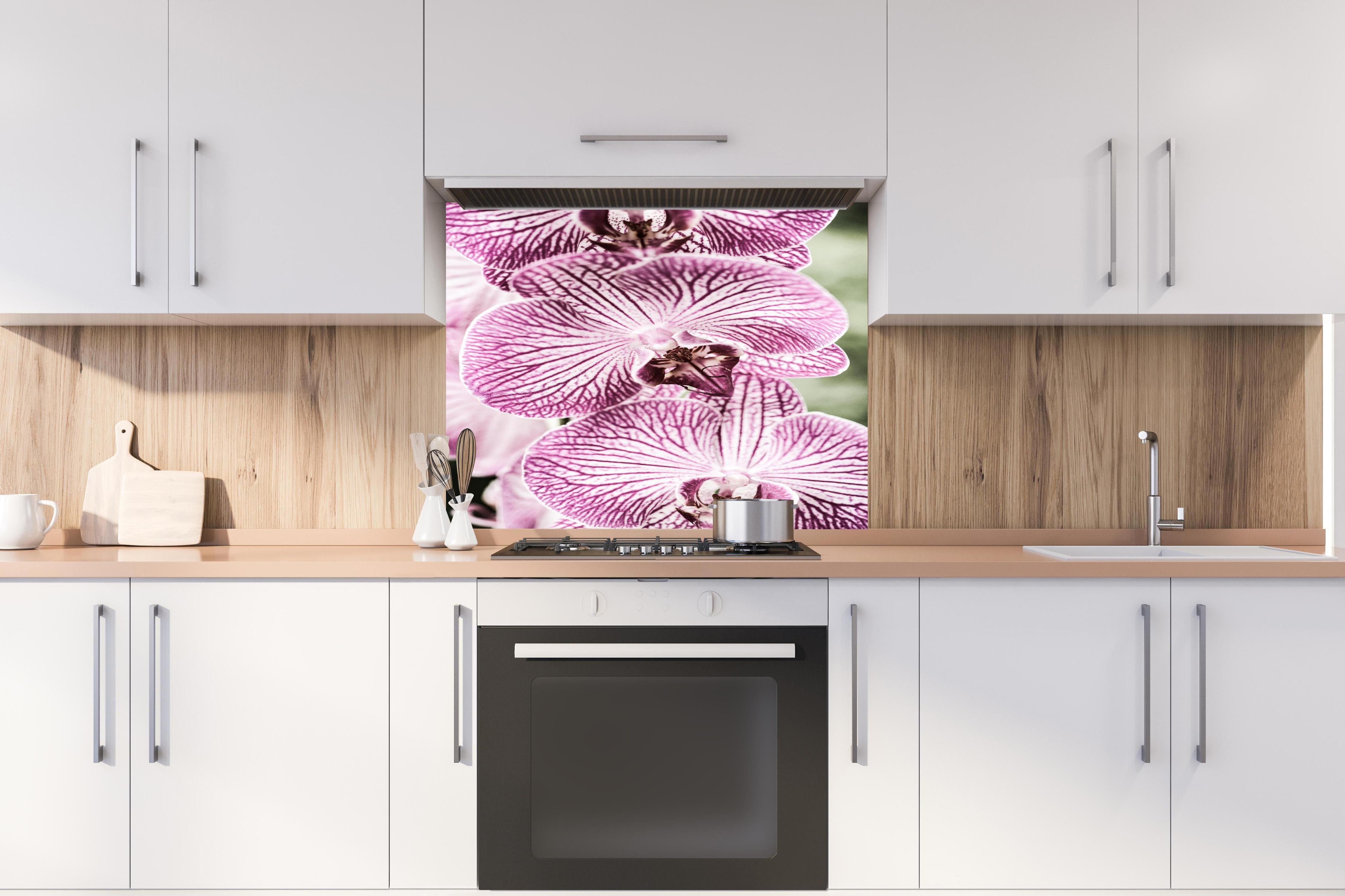 Spritzschutz - Detailreiche Orchideen Makroaufnahme in Pink-Lila hinter einem Cerankochfeld zwischen Holz-Kochutensilien
