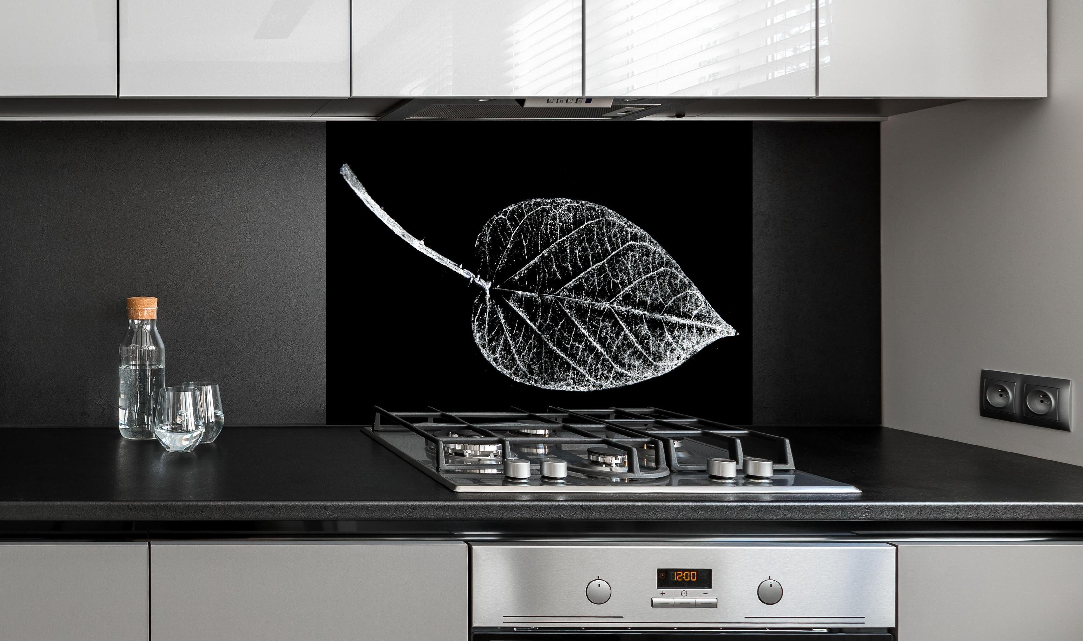 Spritzschutz - Detailreiches Laubblatt in Schwarz und Weiß hinter einem Cerankochfeld zwischen Holz-Kochutensilien

