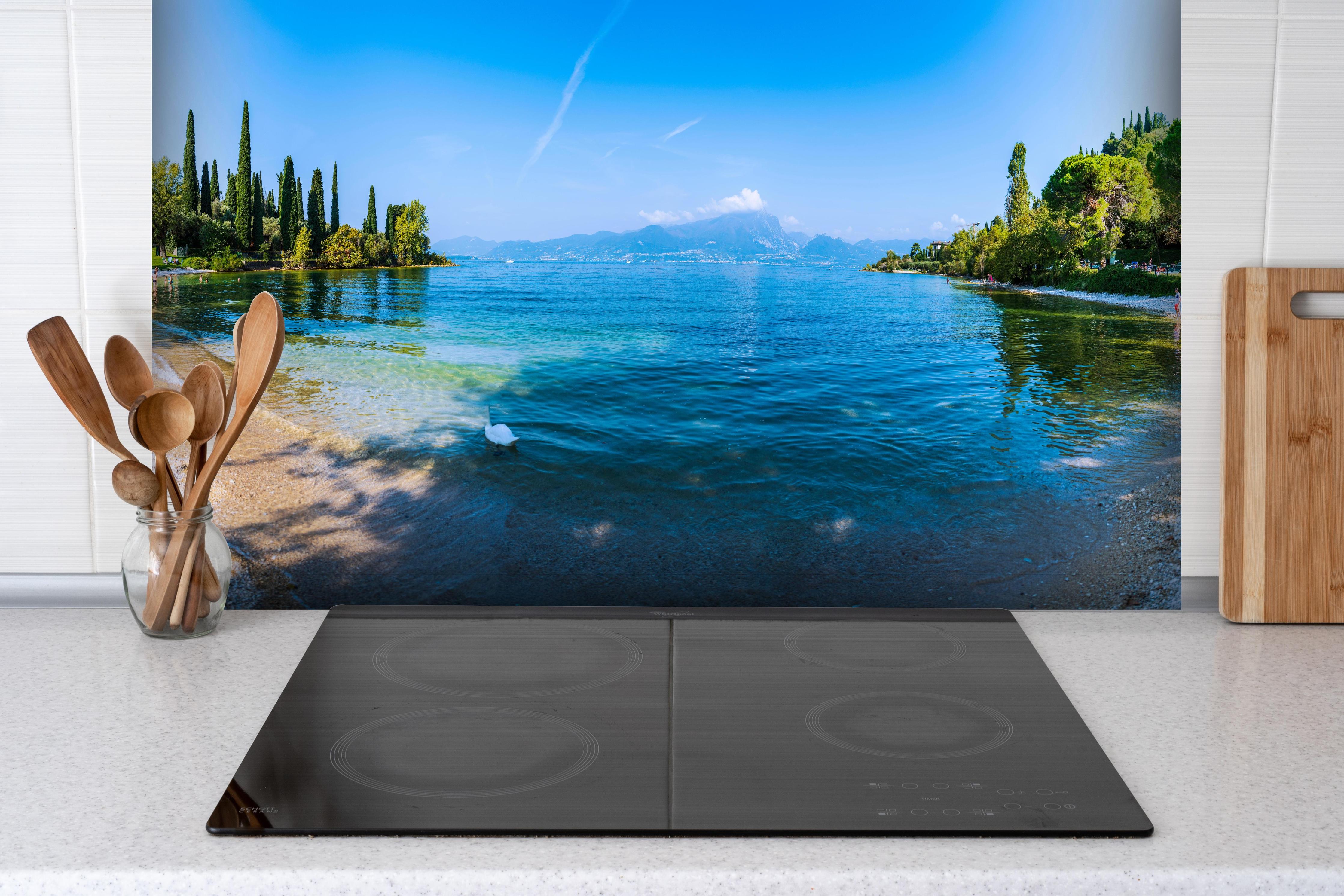 Spritzschutz - Die Schönheit von Punta San Vigilio hinter einem Cerankochfeld zwischen Holz-Kochutensilien
