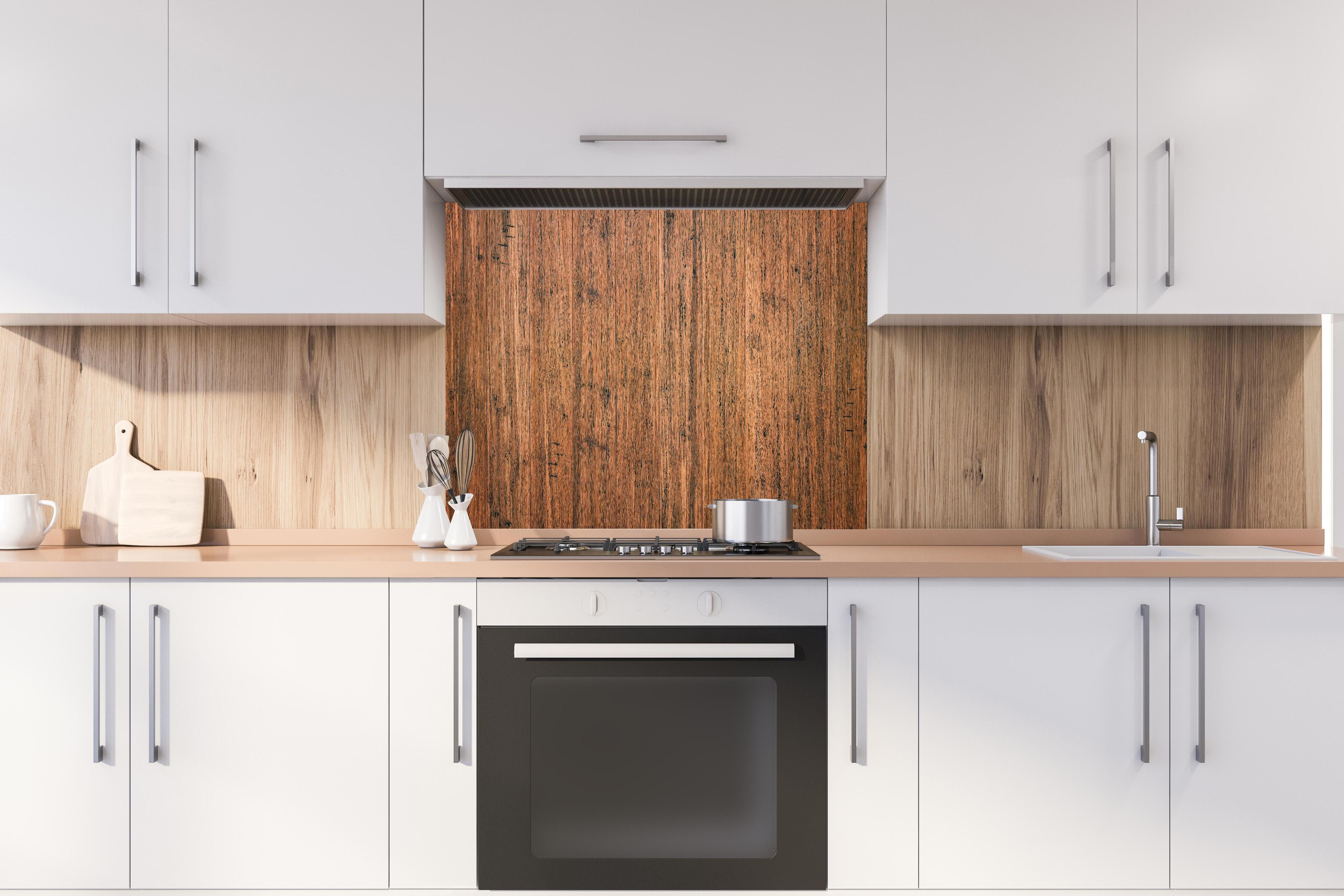 Spritzschutz - Dunkelbraunes rustikales Holzbrett hinter einem Cerankochfeld zwischen Holz-Kochutensilien
