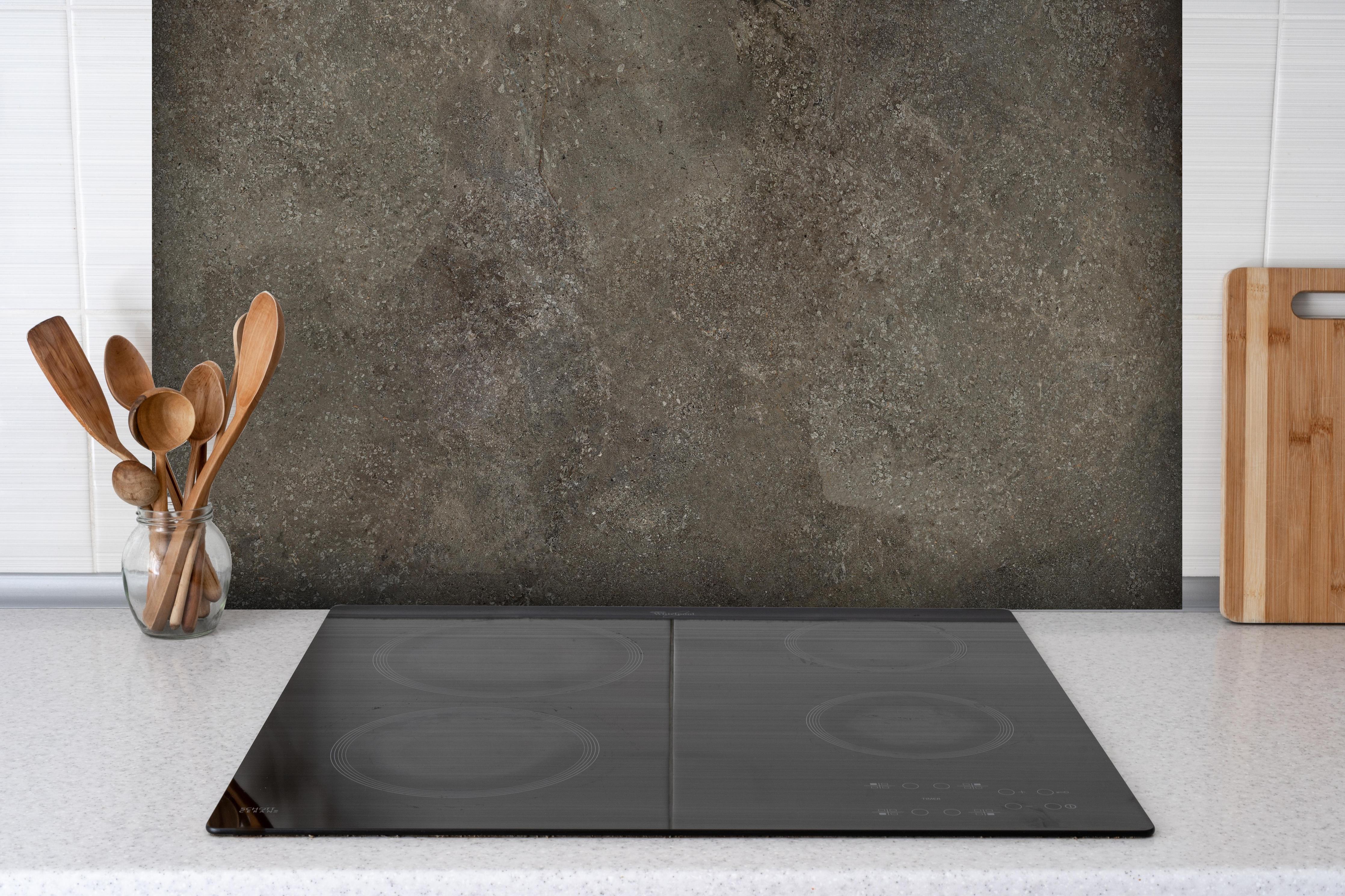 Spritzschutz - Dunkelgrauer schwarzer Schieferhintergrund hinter einem Cerankochfeld zwischen Holz-Kochutensilien
