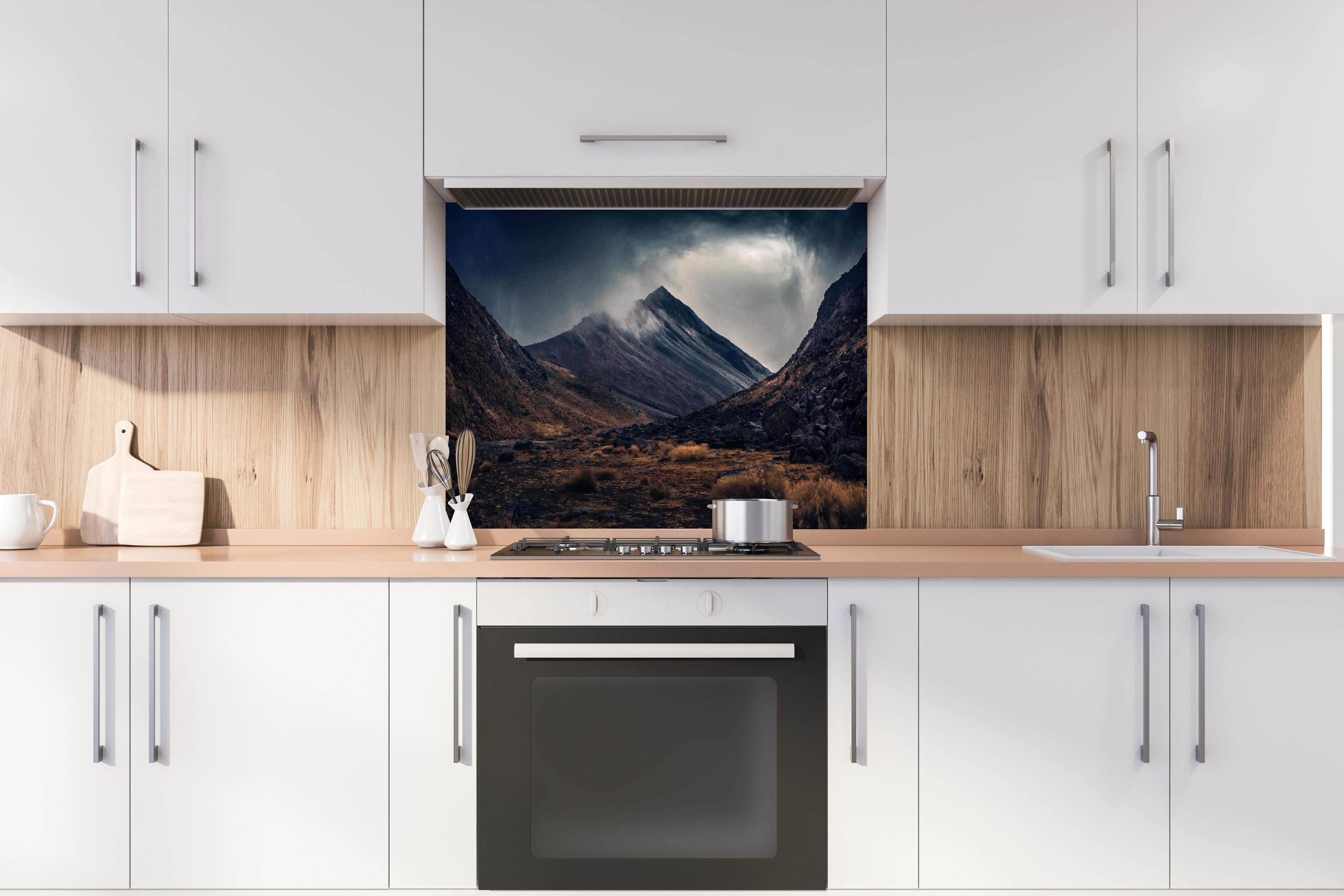 Spritzschutz - Dunkle Wolken Aufziehend über Bergspitze hinter einem Cerankochfeld zwischen Holz-Kochutensilien
