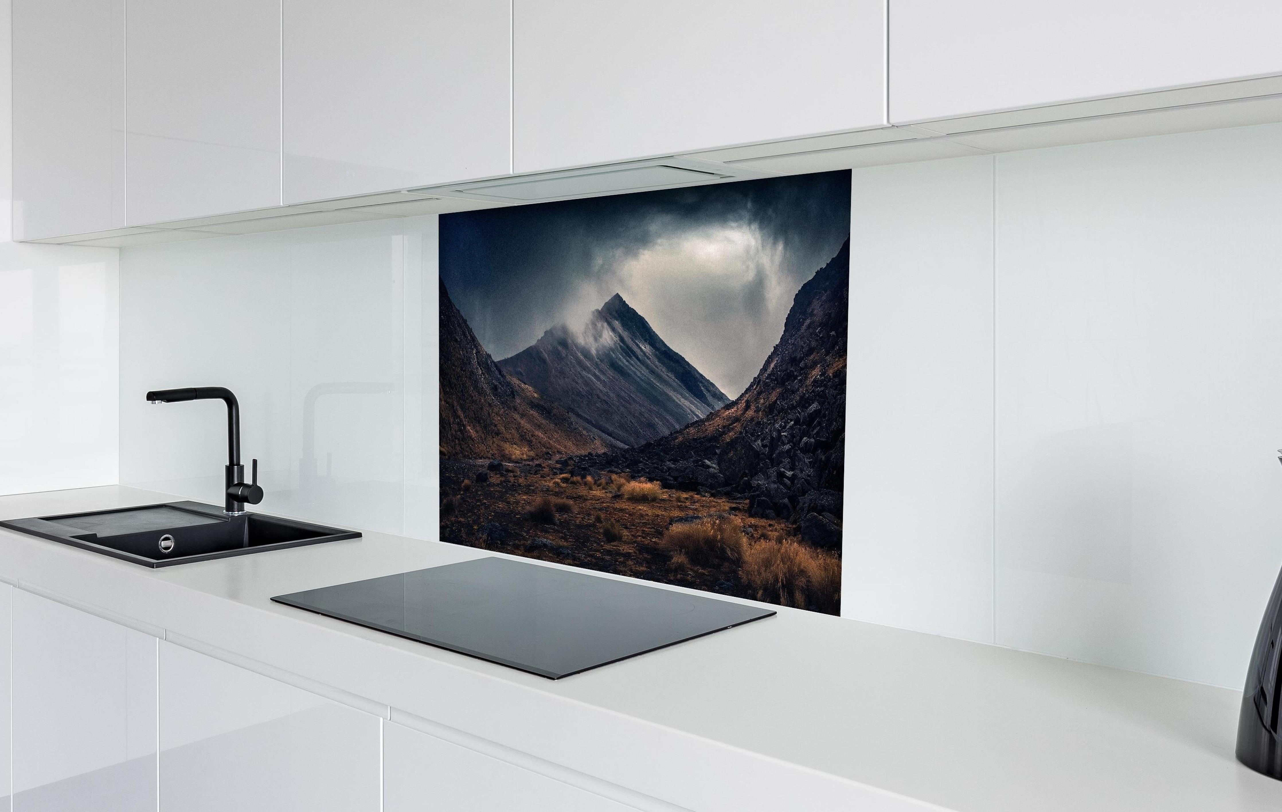 Spritzschutz - Dunkle Wolken Aufziehend über Bergspitze hinter einem Cerankochfeld zwischen Holz-Kochutensilien
