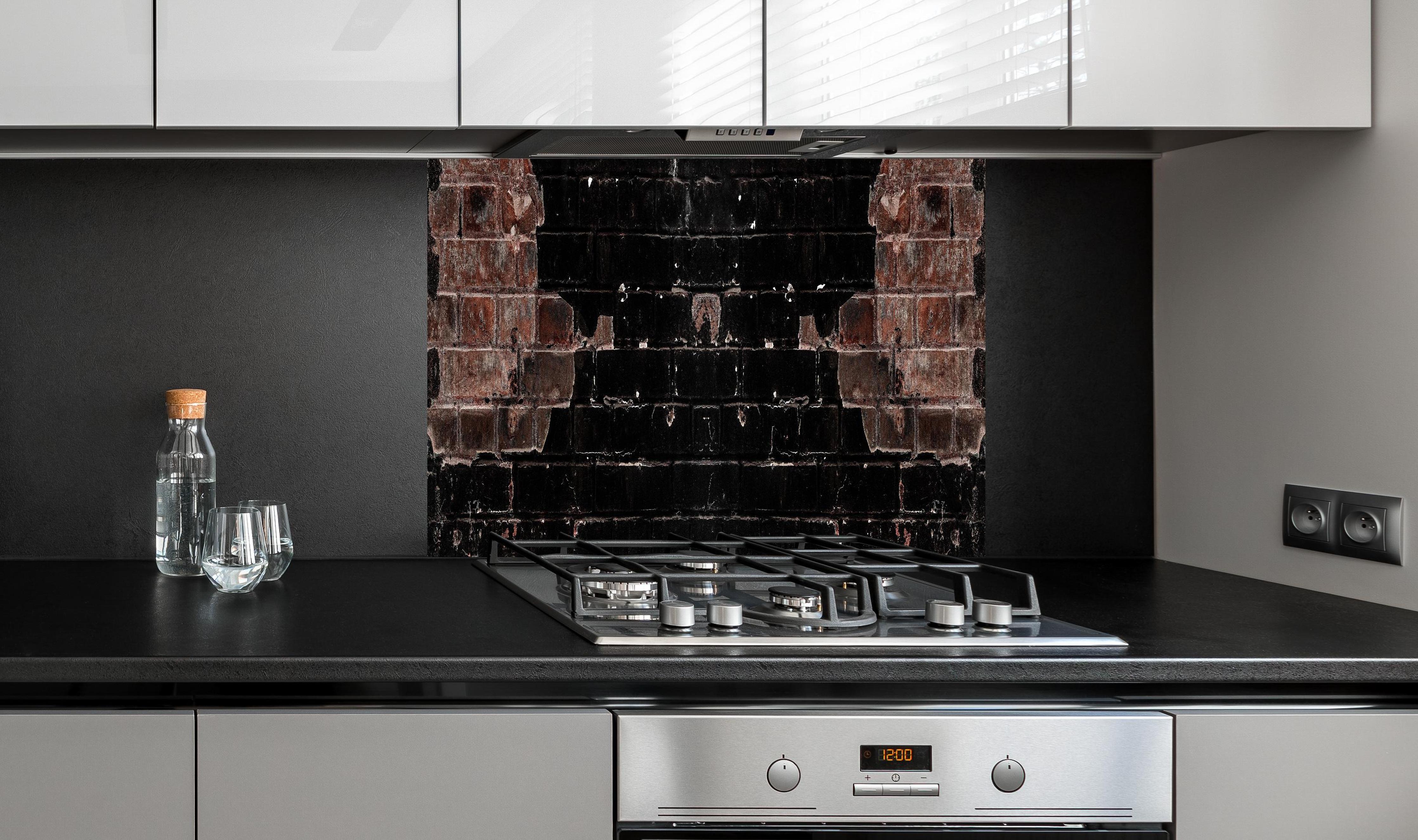 Spritzschutz - Dunkle beschädigte Ziegelwand hinter einem Cerankochfeld zwischen Holz-Kochutensilien
