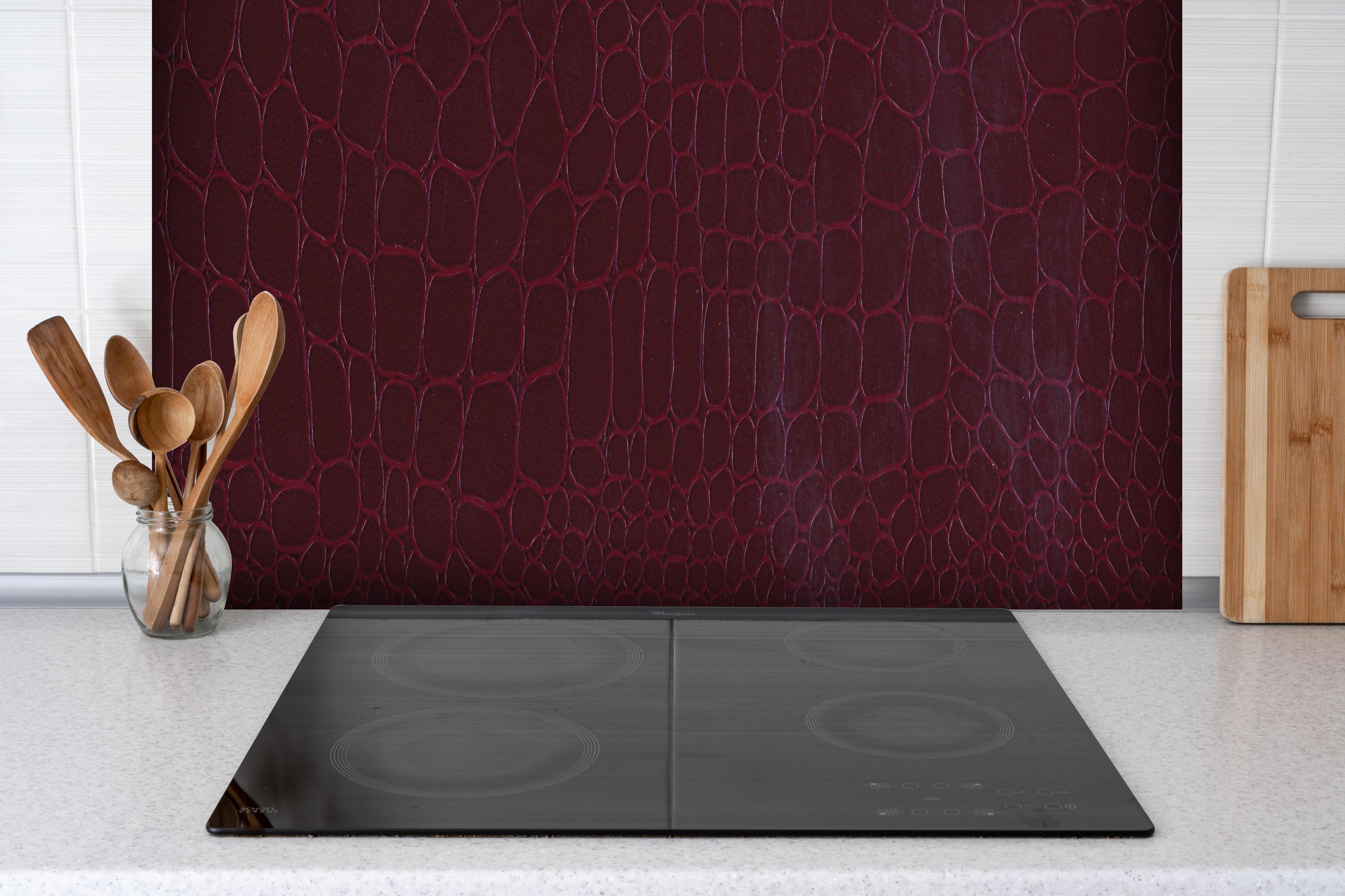 Spritzschutz - Edle rote Krokodil Lederimitation hinter einem Cerankochfeld zwischen Holz-Kochutensilien
