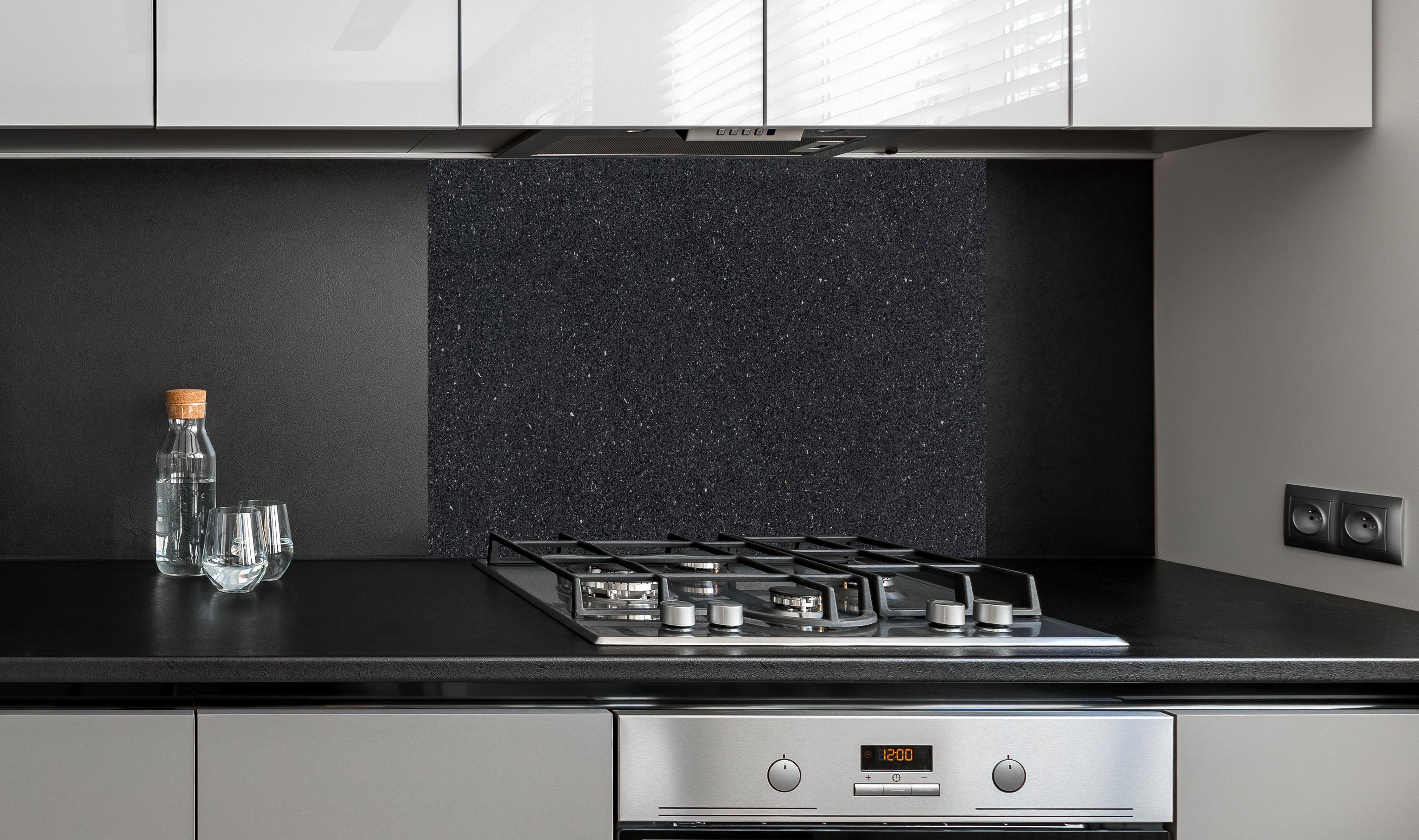 Spritzschutz - Edle schwarze Granite Marmor-Textur hinter einem Cerankochfeld zwischen Holz-Kochutensilien
