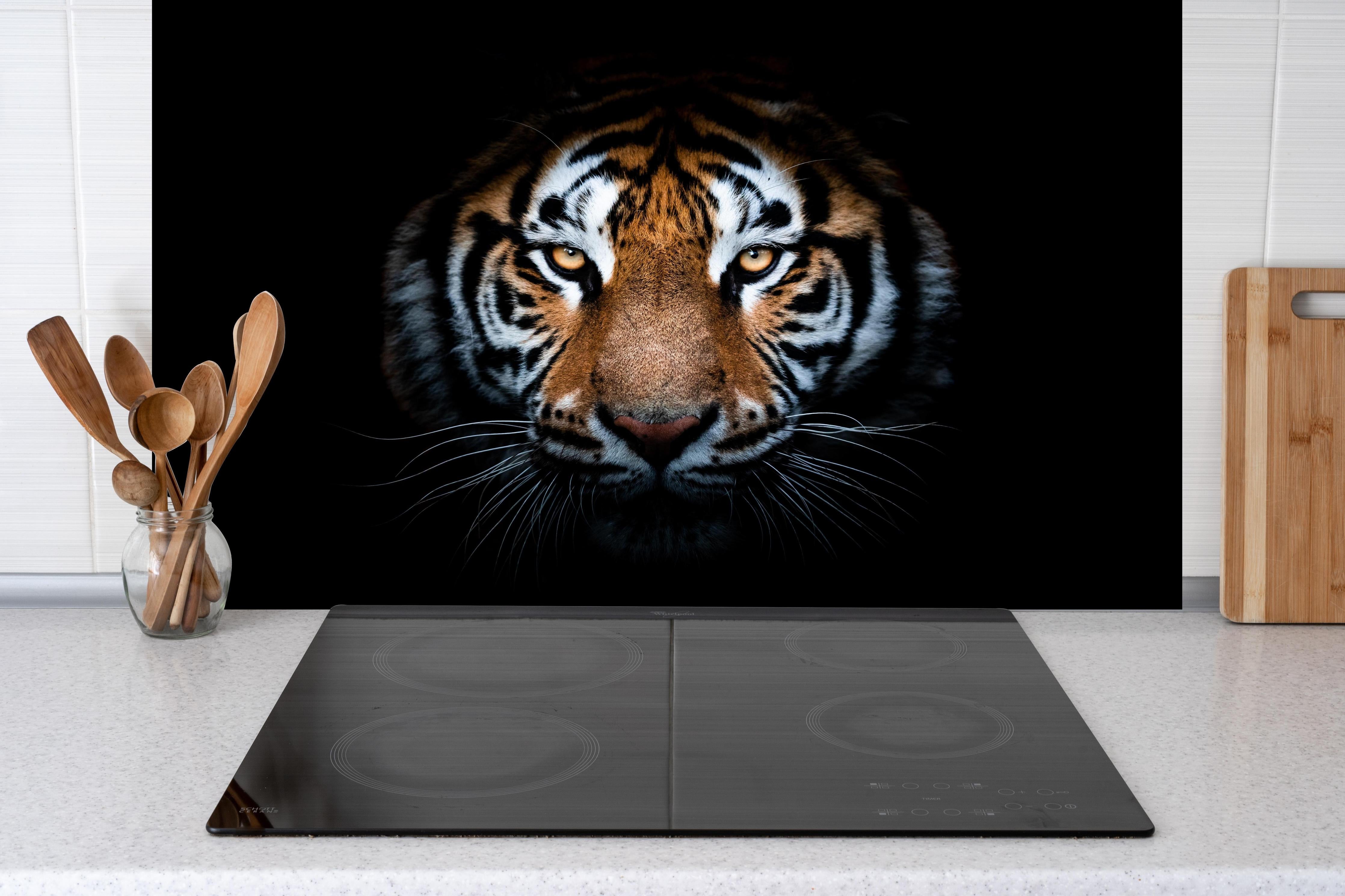 Spritzschutz - Eindrucksvolles Tigergesicht vor Schwarz hinter einem Cerankochfeld zwischen Holz-Kochutensilien

