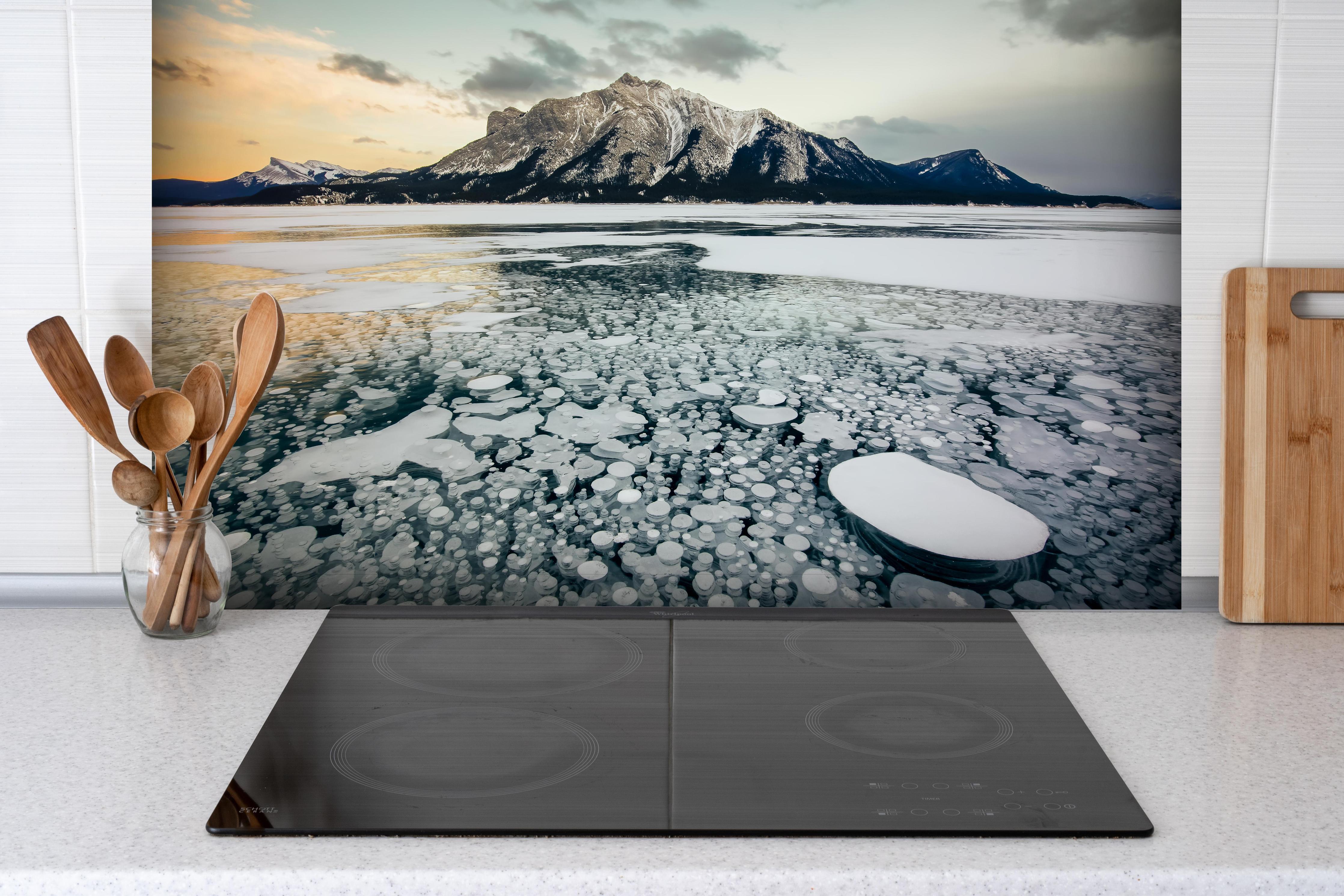 Spritzschutz - Eisblasen im gefrorenen Bergsee bei Sonnenuntergang hinter einem Cerankochfeld zwischen Holz-Kochutensilien
