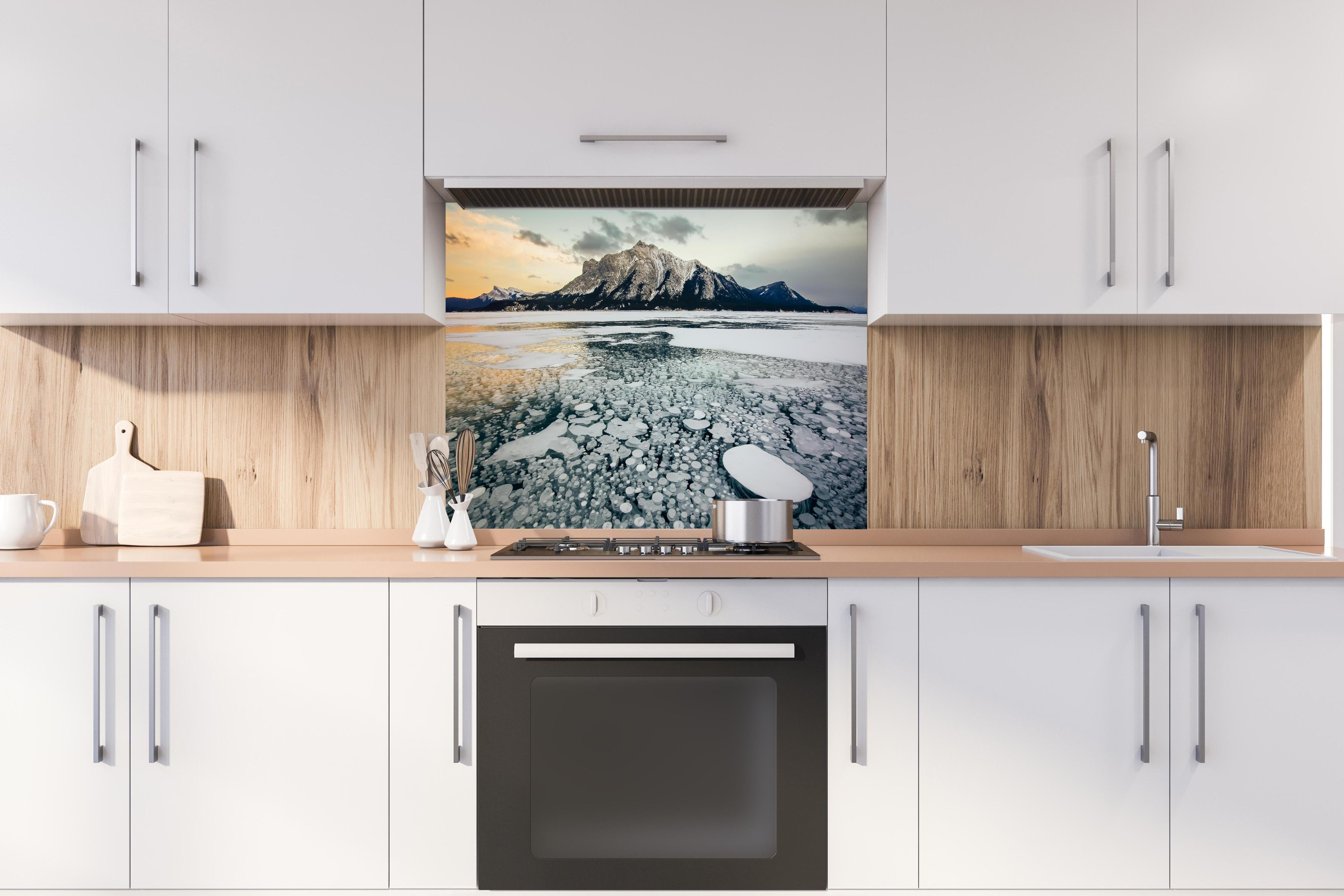 Spritzschutz - Eisblasen im gefrorenen Bergsee bei Sonnenuntergang hinter einem Cerankochfeld zwischen Holz-Kochutensilien
