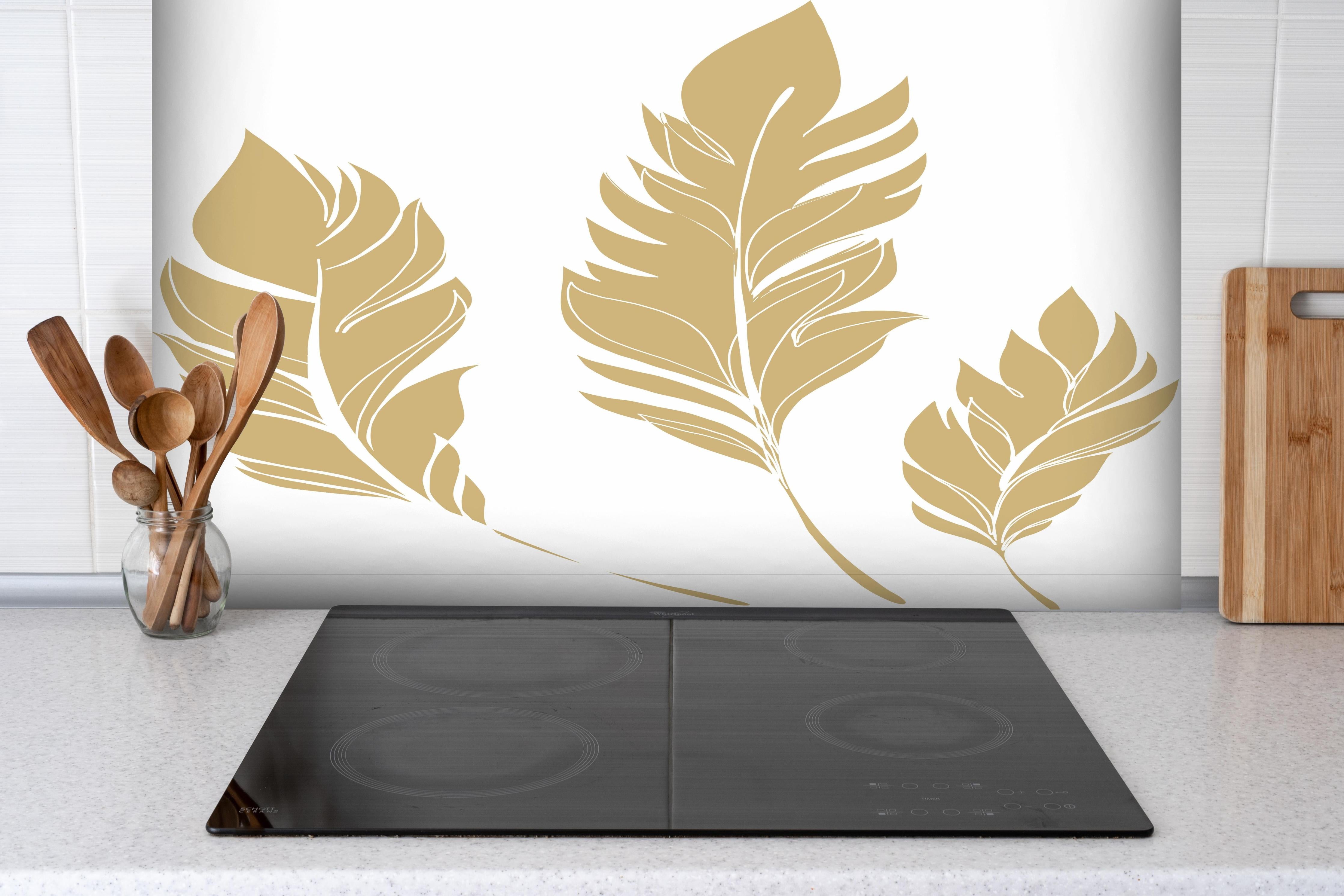 Spritzschutz - Elegante Goldfarbene Feder-Formen Set hinter einem Cerankochfeld zwischen Holz-Kochutensilien
