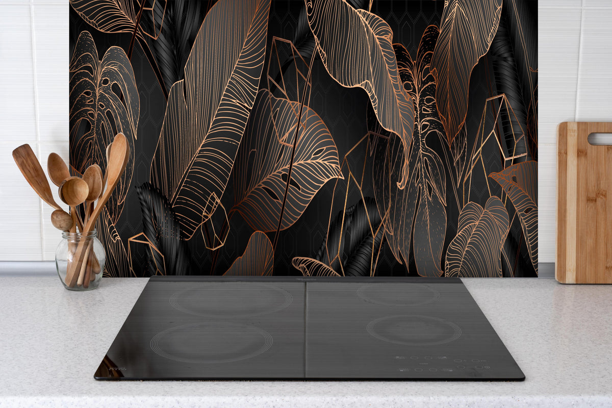 Spritzschutz - Elegante bronzene Blattlinien auf Schwarz hinter einem Cerankochfeld zwischen Holz-Kochutensilien
