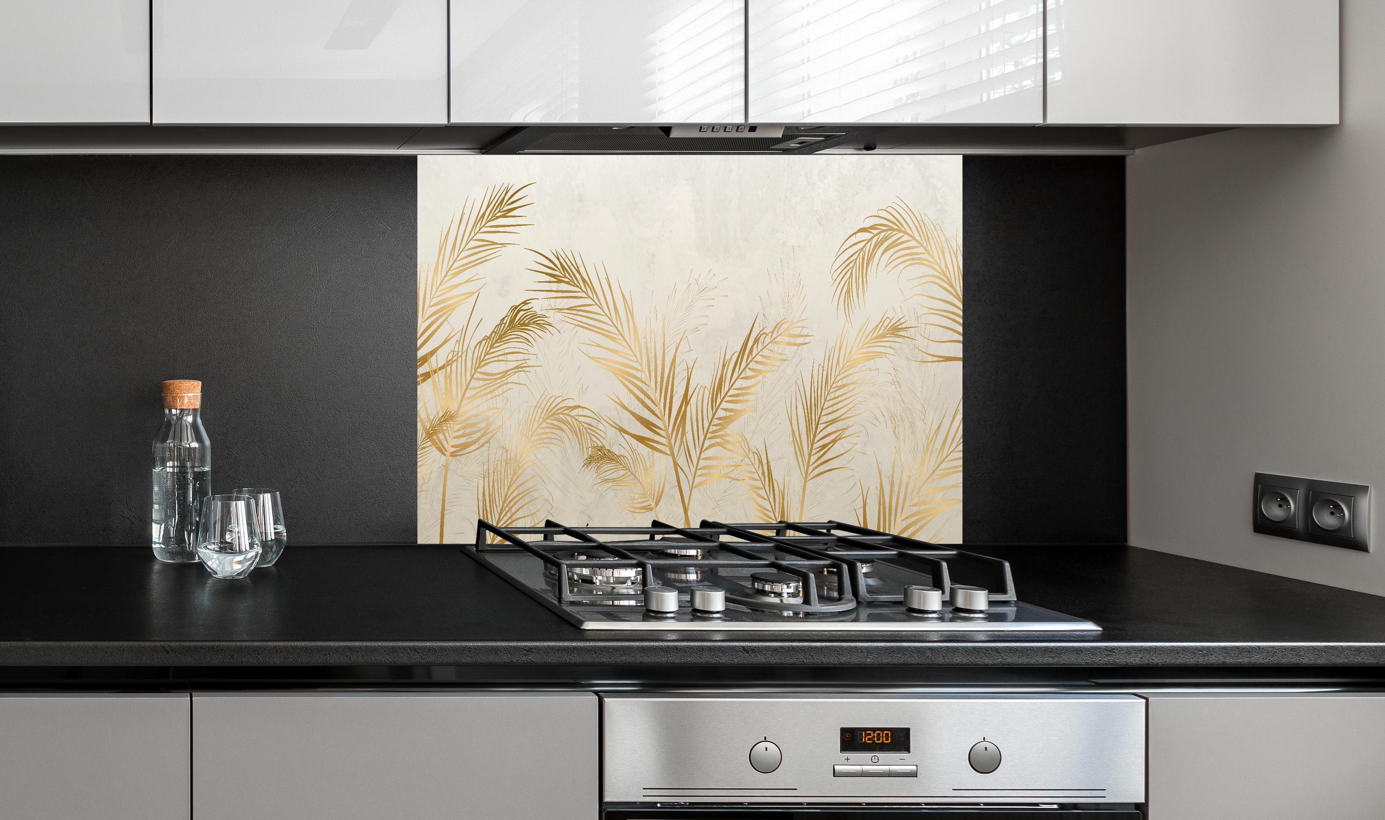 Spritzschutz - Elegante goldene Palmwedel auf hellem Grund hinter einem Cerankochfeld zwischen Holz-Kochutensilien
