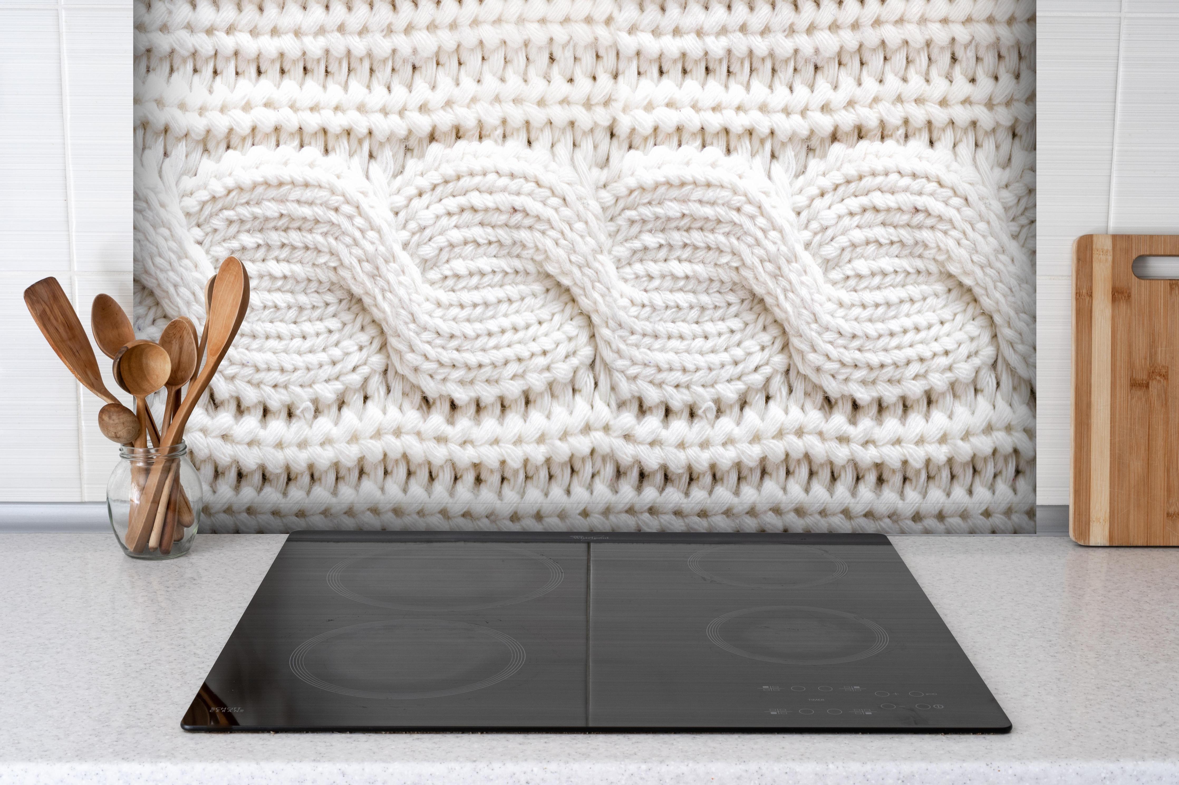 Spritzschutz - Elegante weiße Stricktextur aus Wolle hinter einem Cerankochfeld zwischen Holz-Kochutensilien
