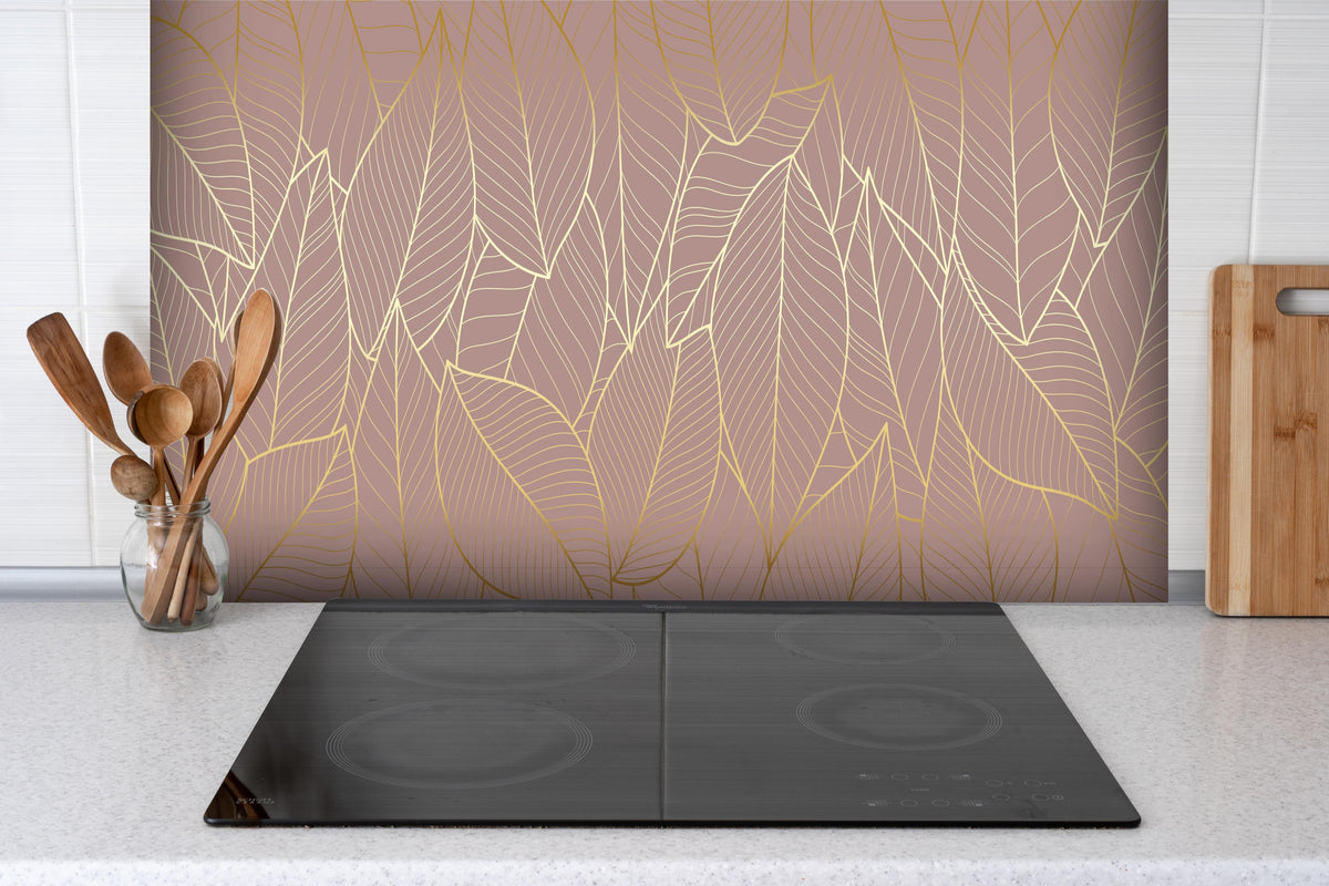 Spritzschutz - Elegantes Blattgold-Muster auf Taupe-Hintergrund hinter einem Cerankochfeld zwischen Holz-Kochutensilien
