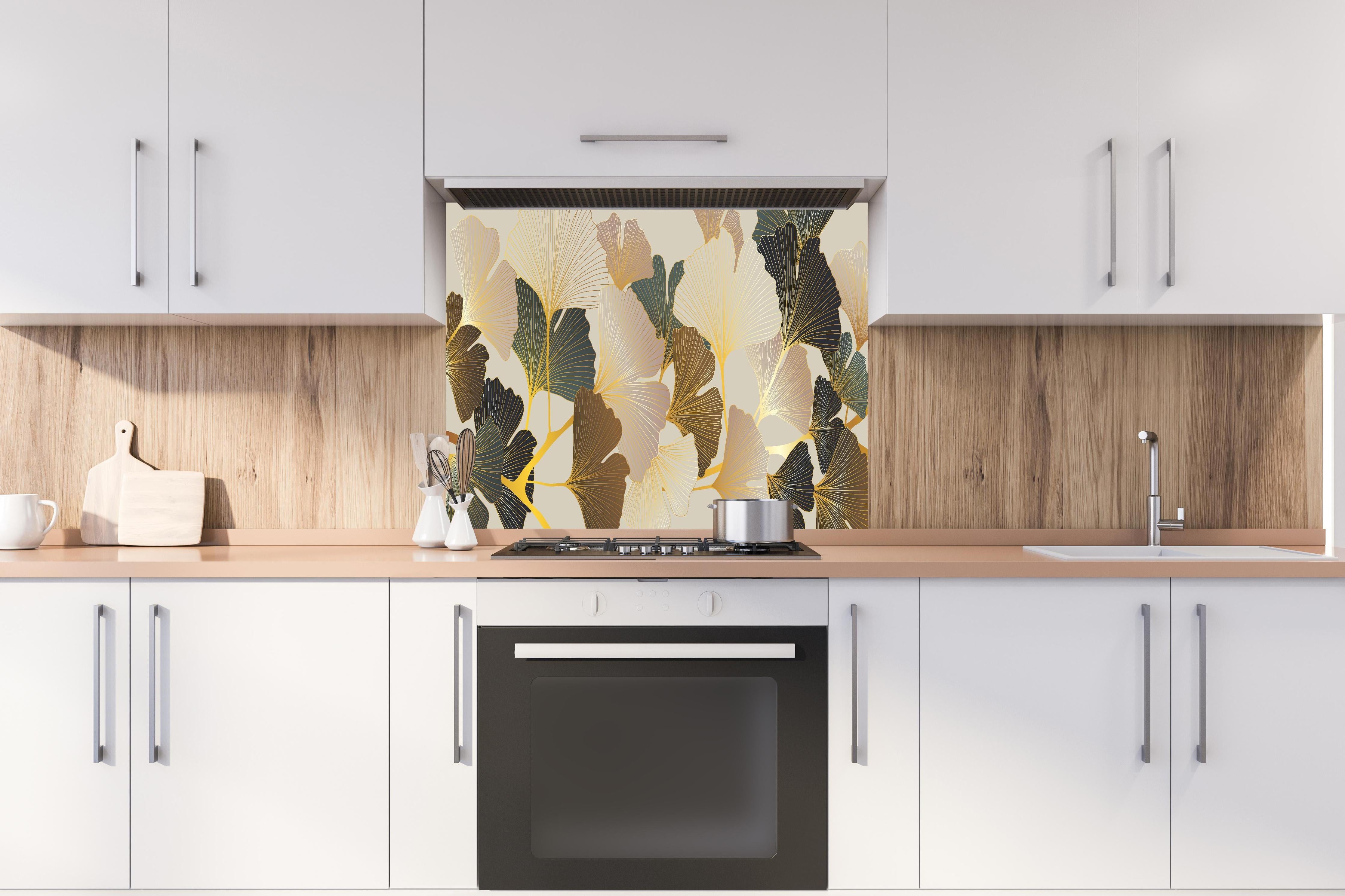 Spritzschutz - Elegantes Ginkgo-Blattmotiv mit goldfarbenen Akzenten hinter einem Cerankochfeld zwischen Holz-Kochutensilien
