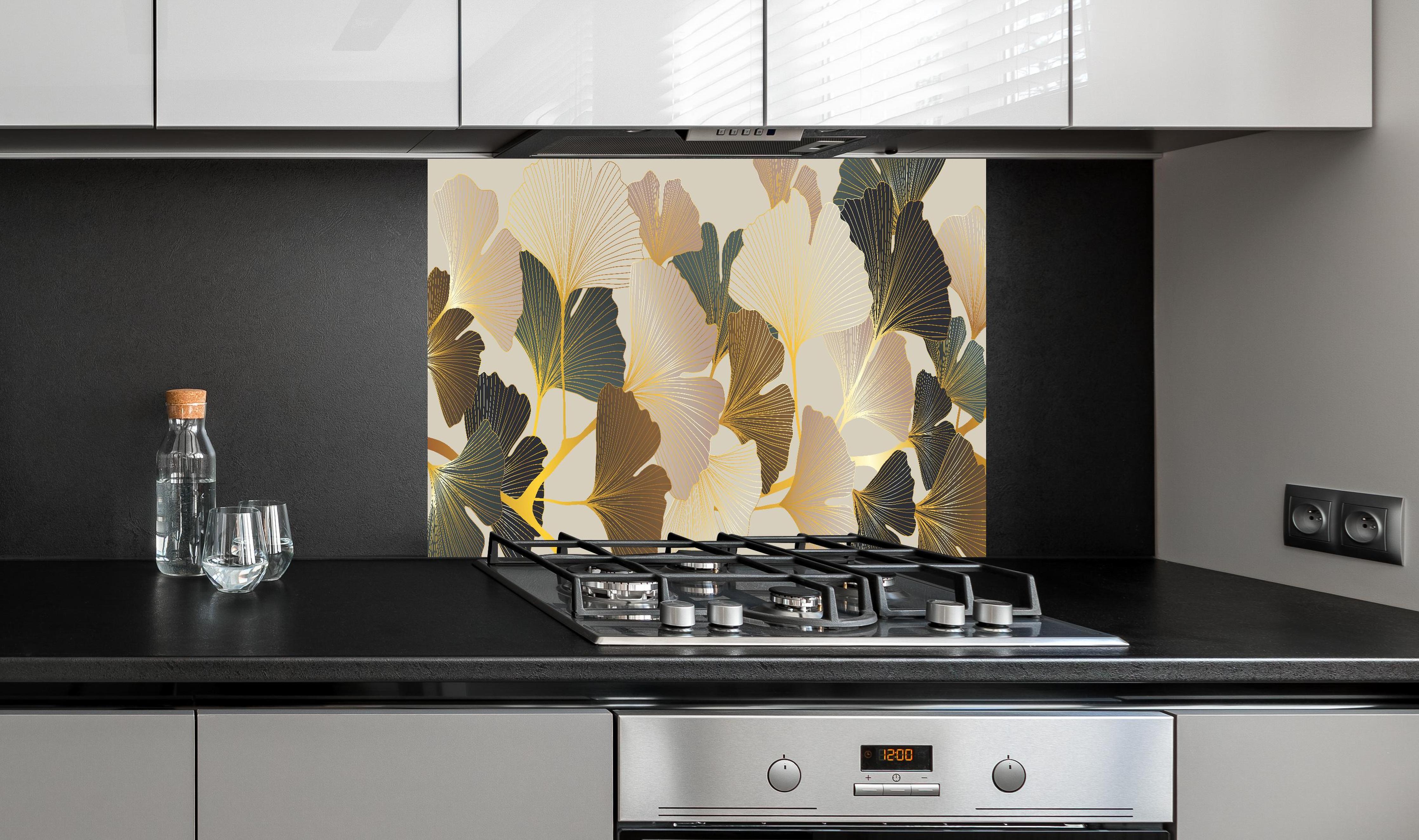 Spritzschutz - Elegantes Ginkgo-Blattmotiv mit goldfarbenen Akzenten hinter einem Cerankochfeld zwischen Holz-Kochutensilien
