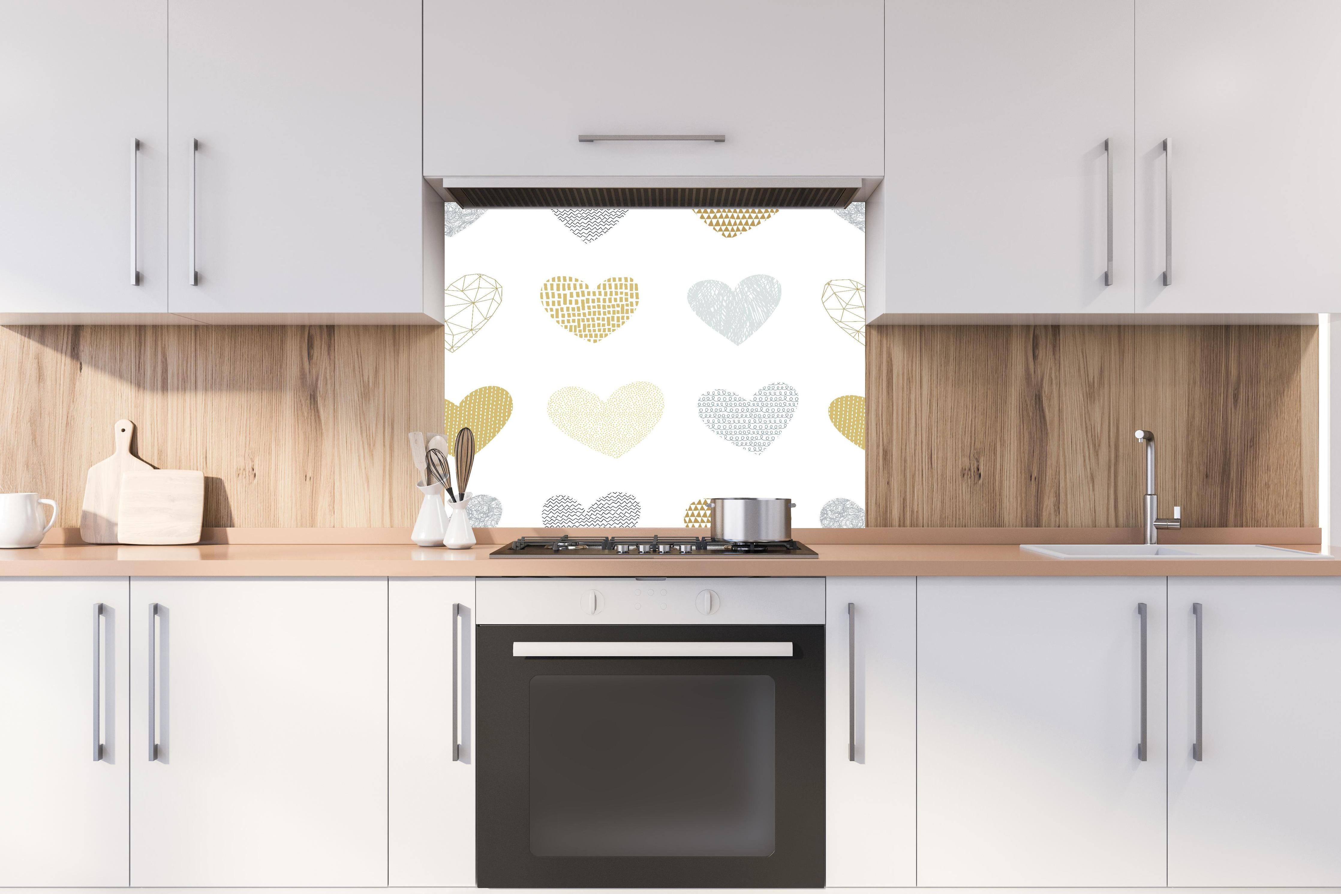 Spritzschutz - Elegantes Herz-Muster in Gold und Grau hinter einem Cerankochfeld zwischen Holz-Kochutensilien

