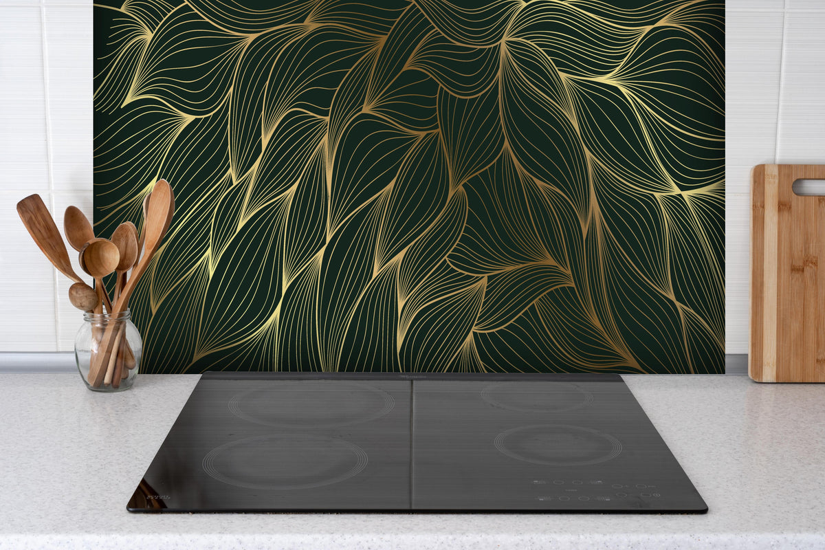 Spritzschutz - Elegantes Wellenmuster in Gold und Dunkelgrün hinter einem Cerankochfeld zwischen Holz-Kochutensilien

