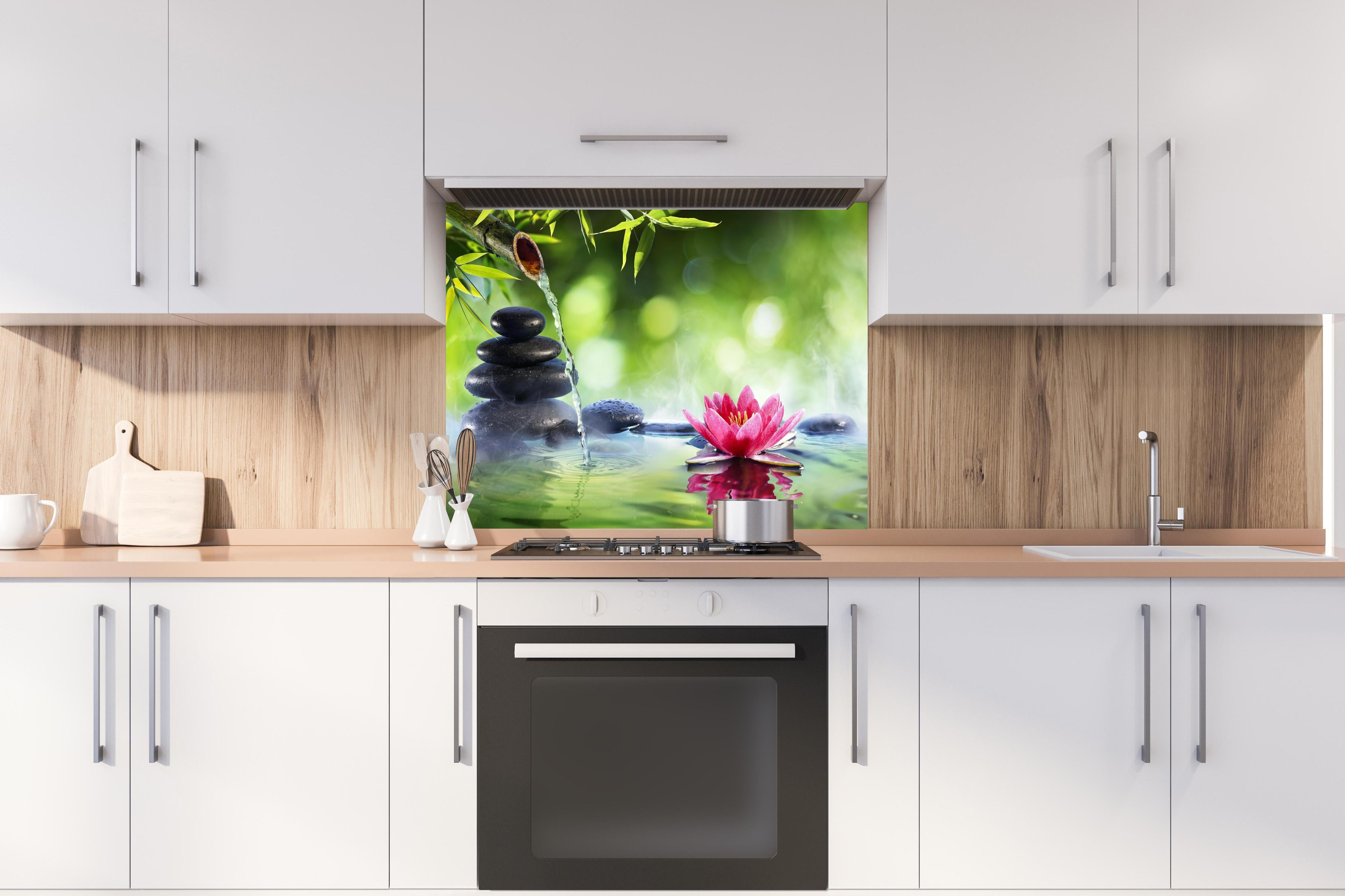 Spritzschutz - Entspannende Zen-Steine und pinkfarbene Lotusblüte hinter einem Cerankochfeld zwischen Holz-Kochutensilien
