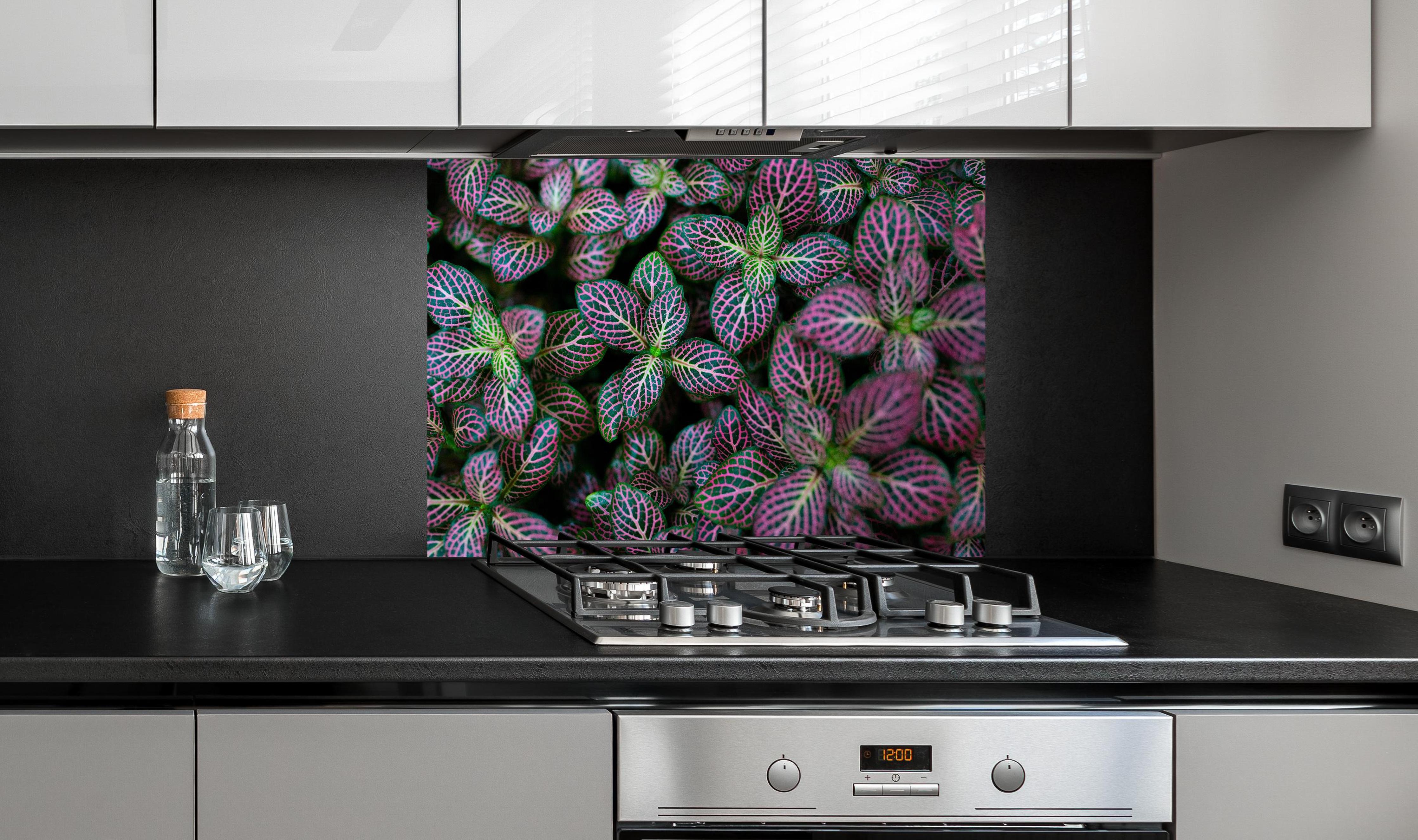 Spritzschutz - Exotische Blätter Textur in Bunt hinter einem Cerankochfeld zwischen Holz-Kochutensilien
