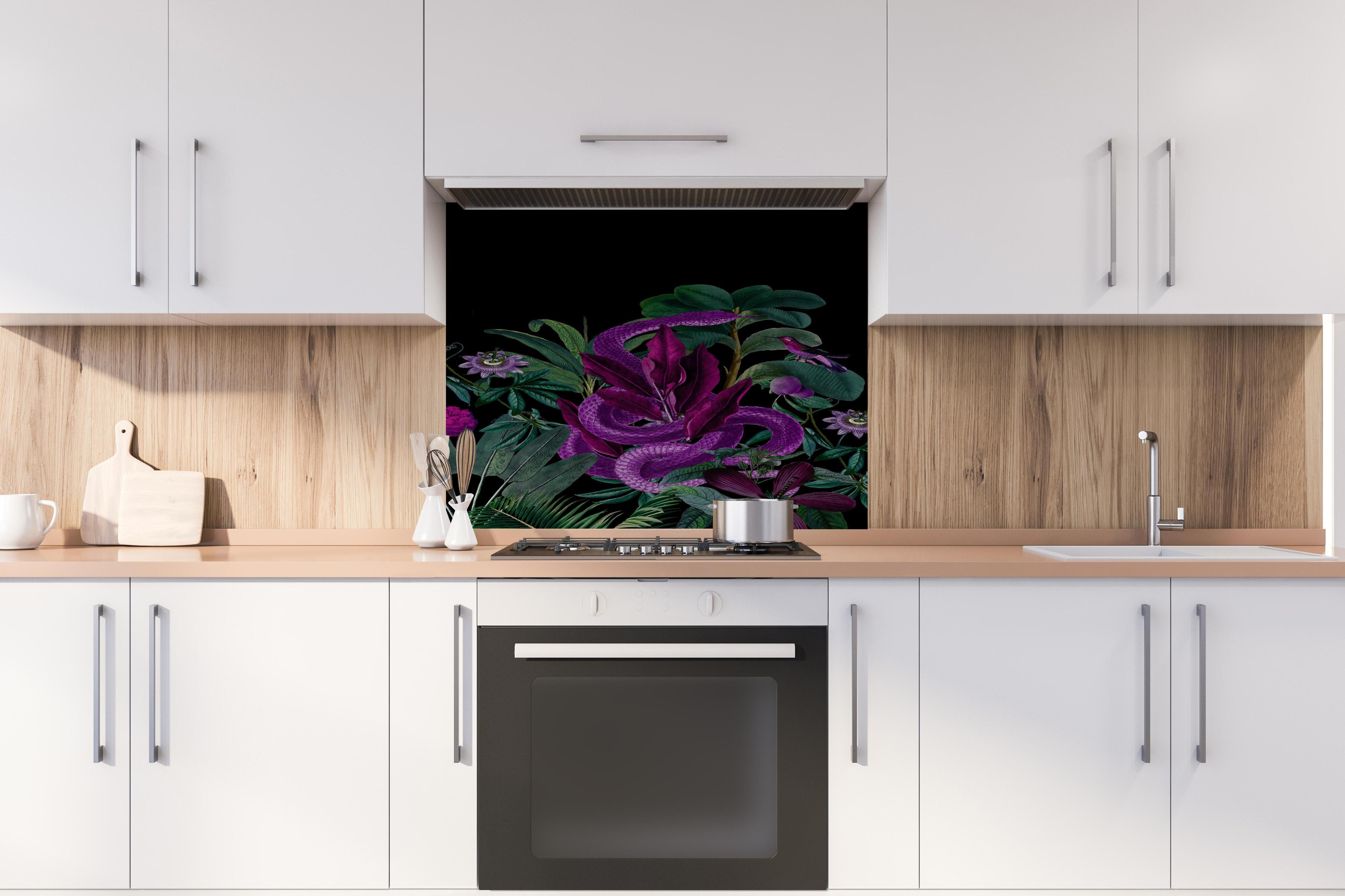 Spritzschutz - Exotischer Schlangenprint in Lila und Grün hinter einem Cerankochfeld zwischen Holz-Kochutensilien
