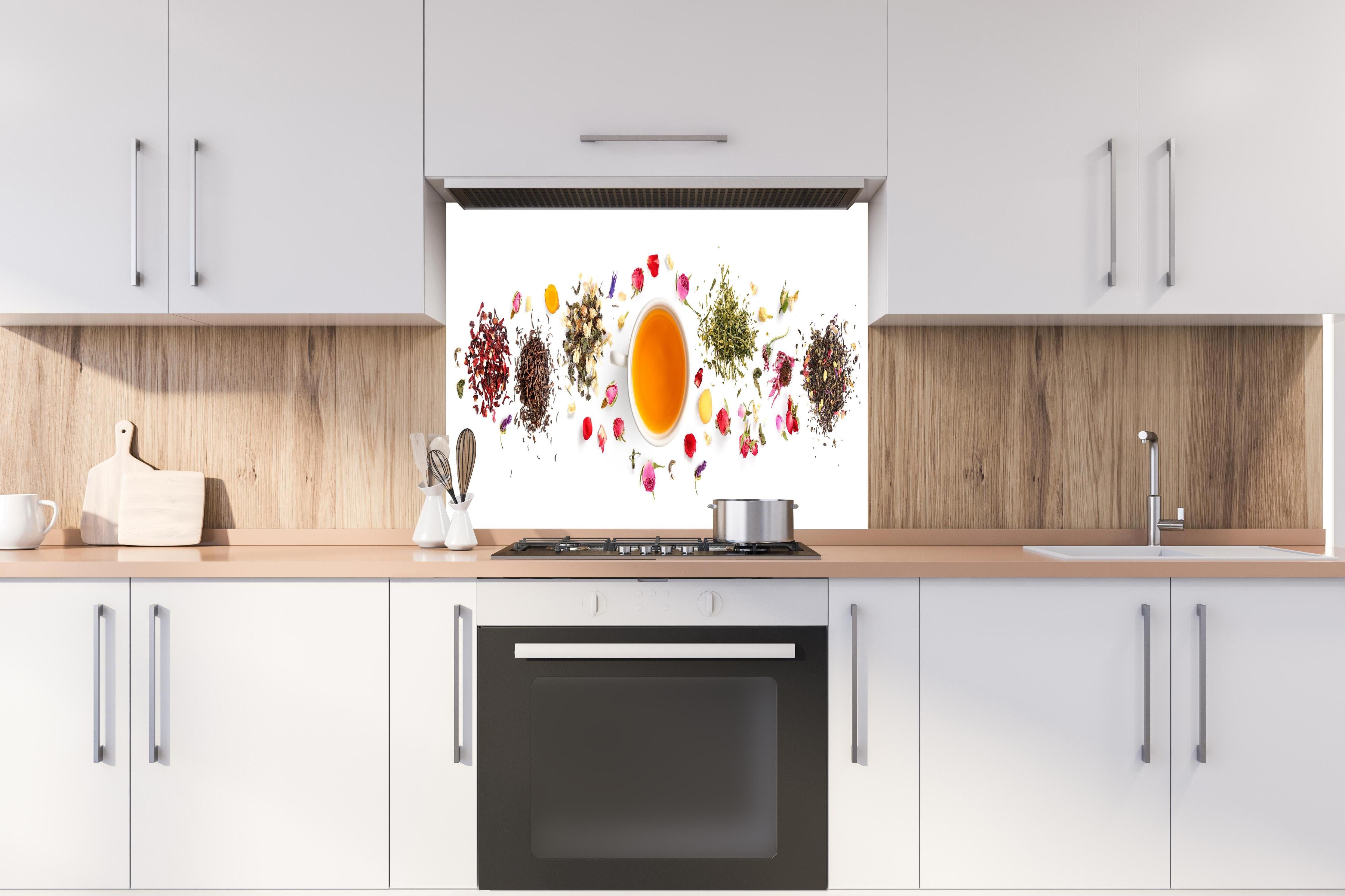 Spritzschutz - Exquisite Teesorten umgeben von Blumen hinter einem Cerankochfeld zwischen Holz-Kochutensilien
