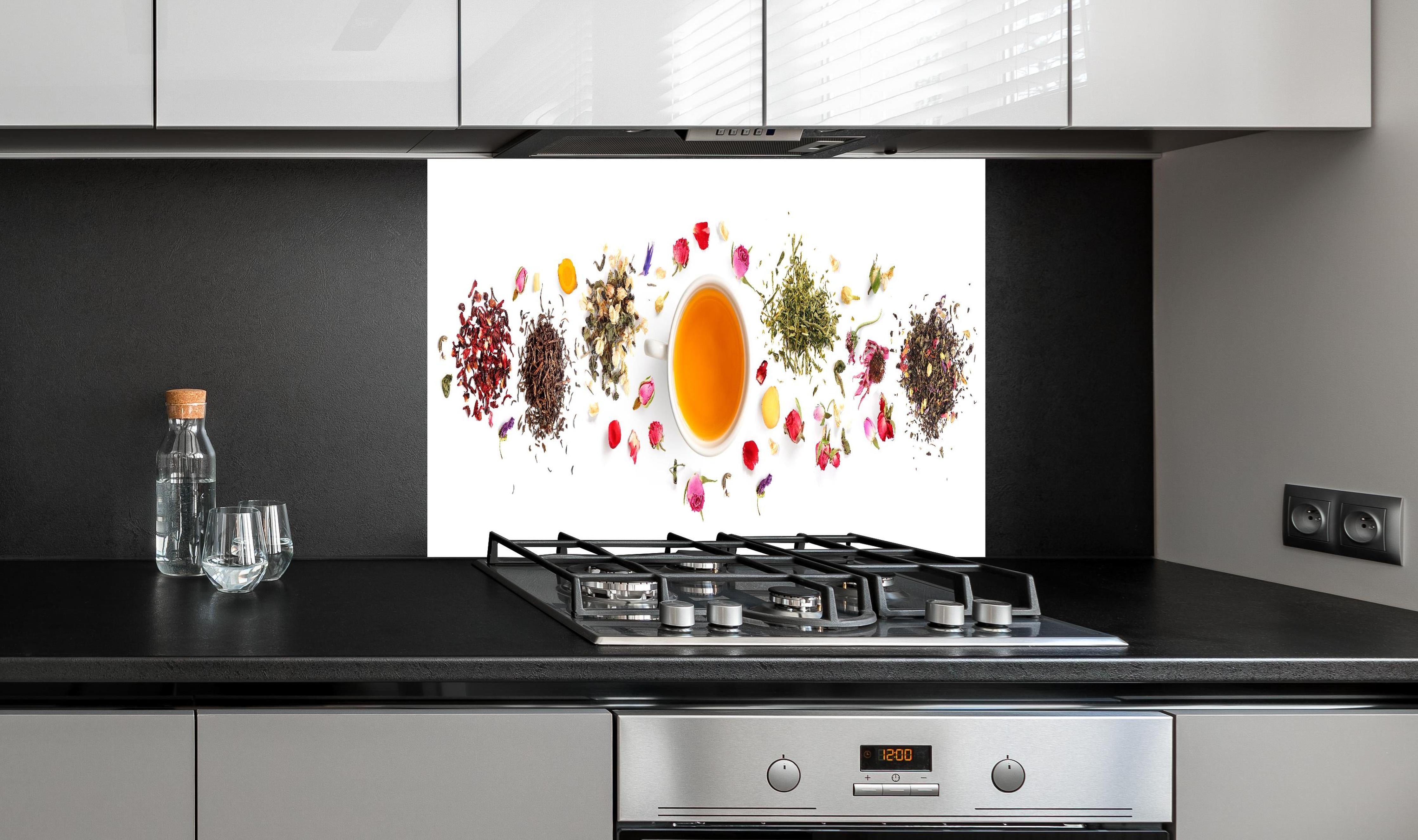 Spritzschutz - Exquisite Teesorten umgeben von Blumen hinter einem Cerankochfeld zwischen Holz-Kochutensilien
