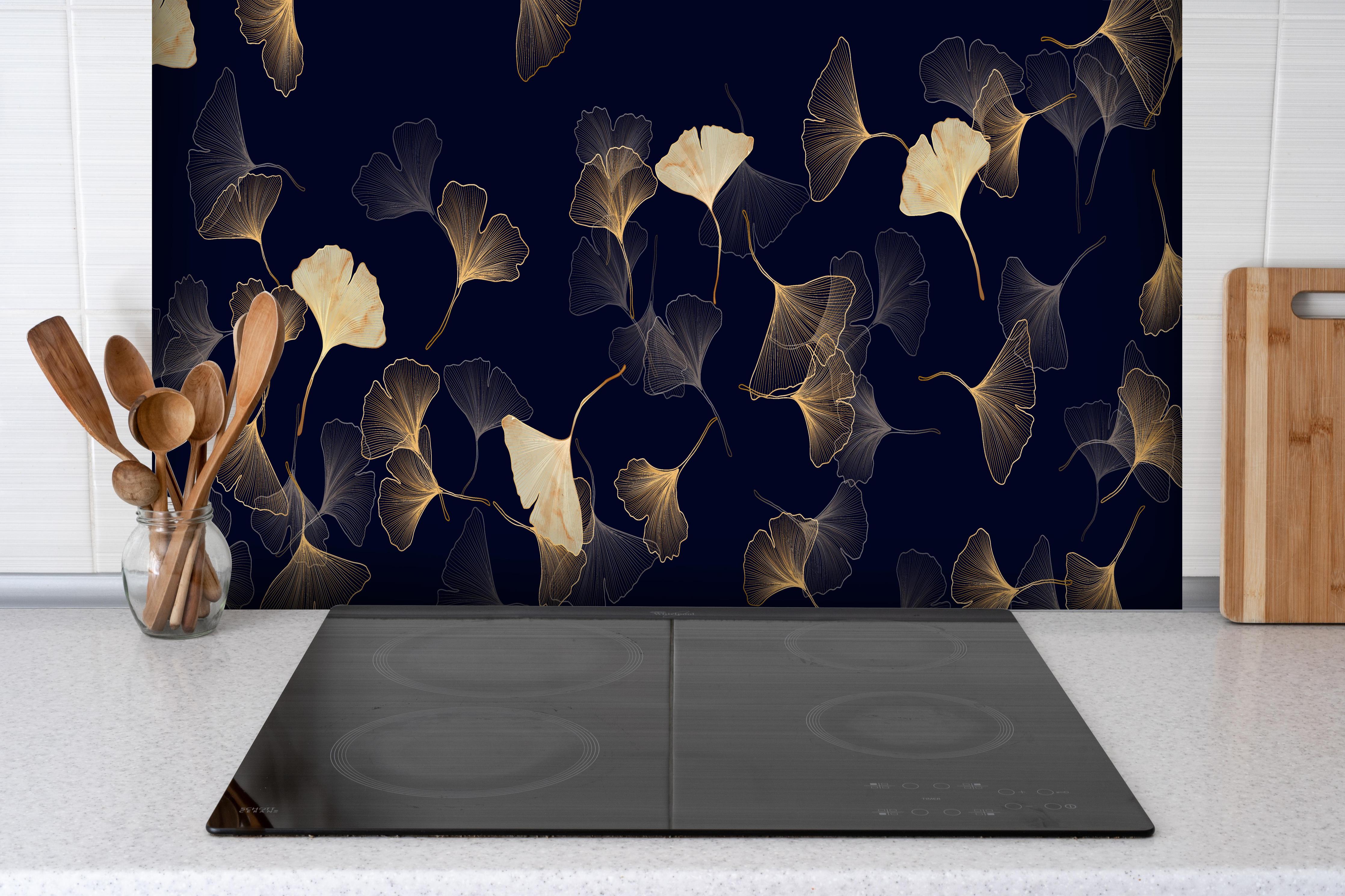 Spritzschutz - Exquisite goldene Ginkgo Blätter auf dunklem Hintergrund hinter einem Cerankochfeld zwischen Holz-Kochutensilien
