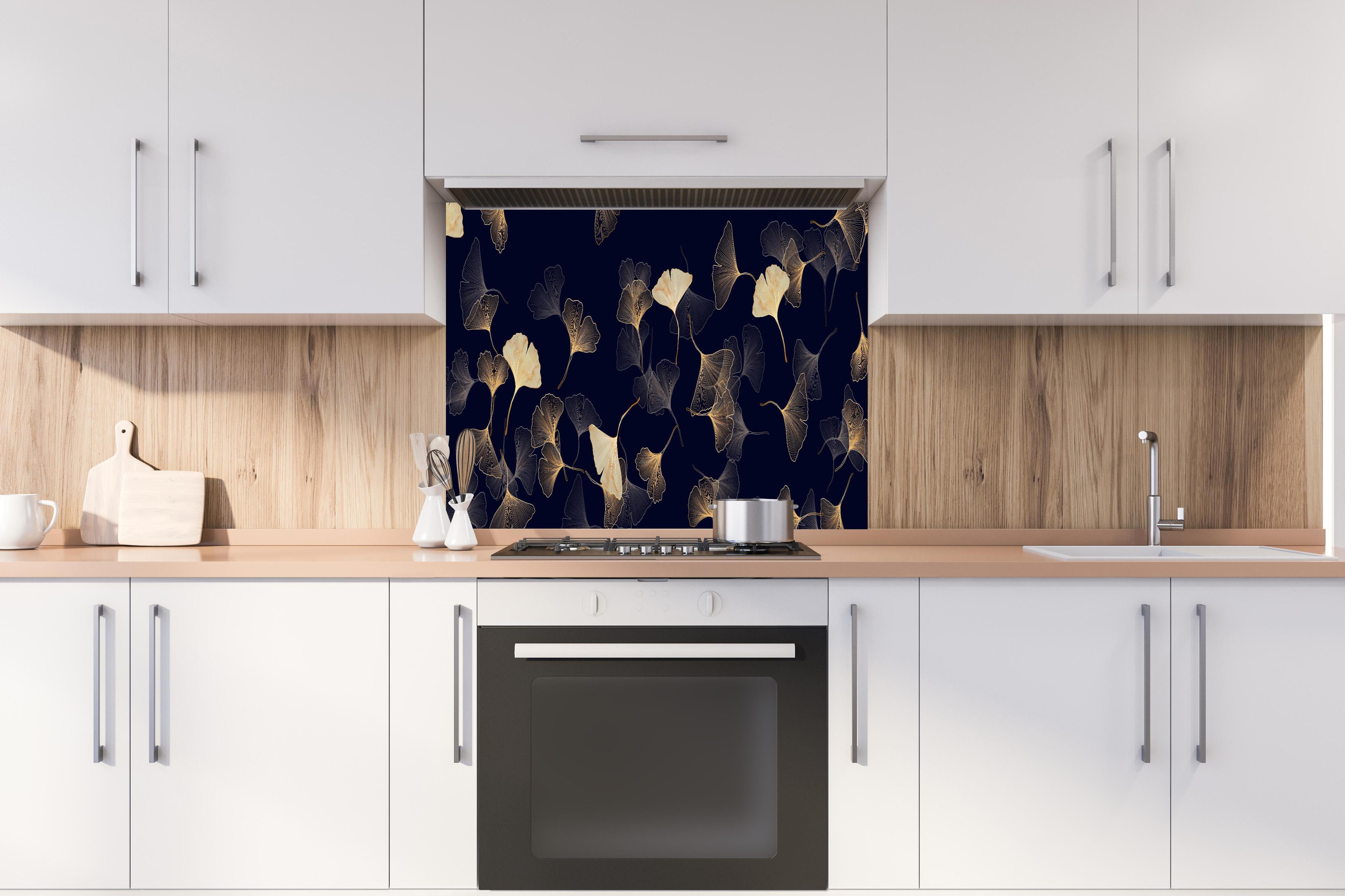 Spritzschutz - Exquisite goldene Ginkgo Blätter auf dunklem Hintergrund hinter einem Cerankochfeld zwischen Holz-Kochutensilien
