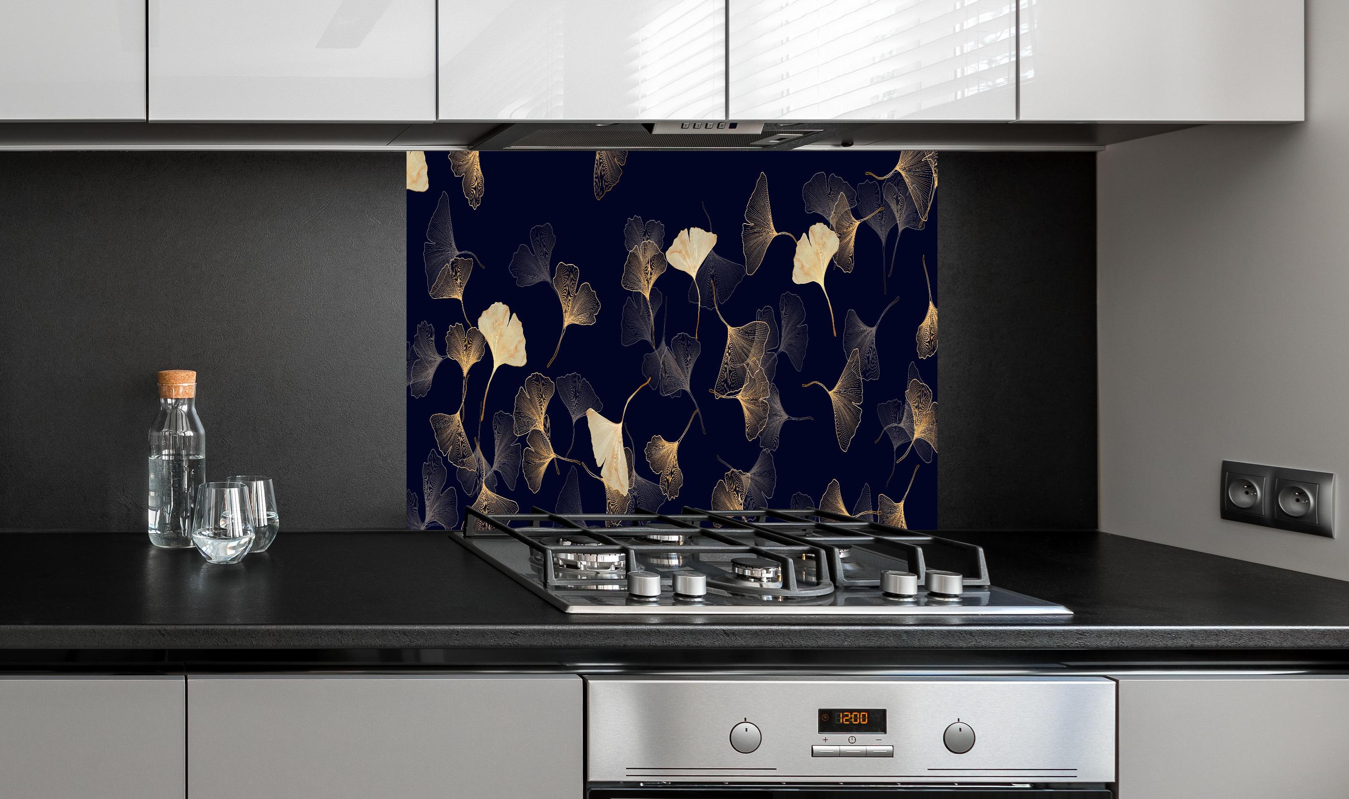 Spritzschutz - Exquisite goldene Ginkgo Blätter auf dunklem Hintergrund hinter einem Cerankochfeld zwischen Holz-Kochutensilien
