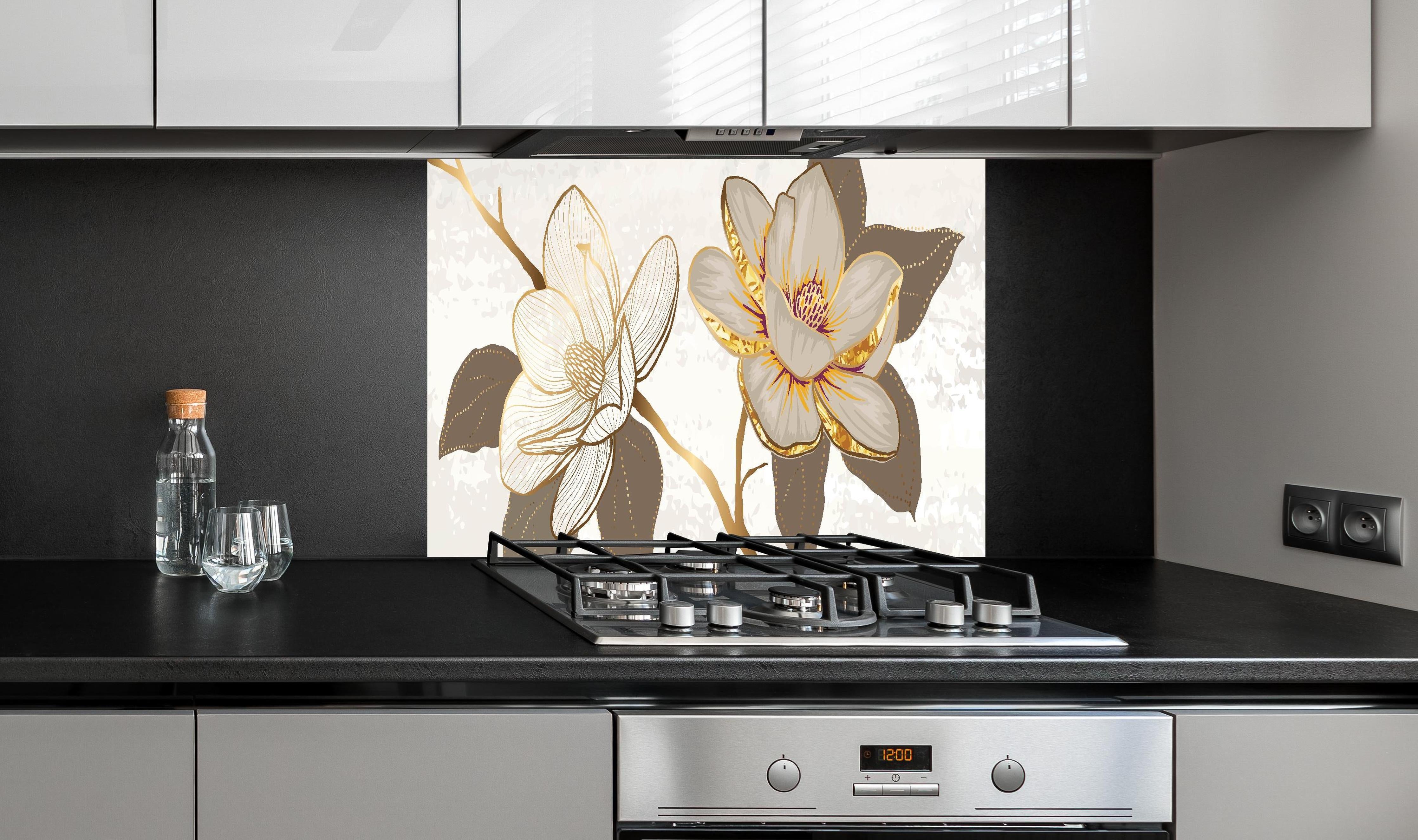 Spritzschutz - Exquisites Magnolienmuster in Gold und Beige hinter einem Cerankochfeld zwischen Holz-Kochutensilien
