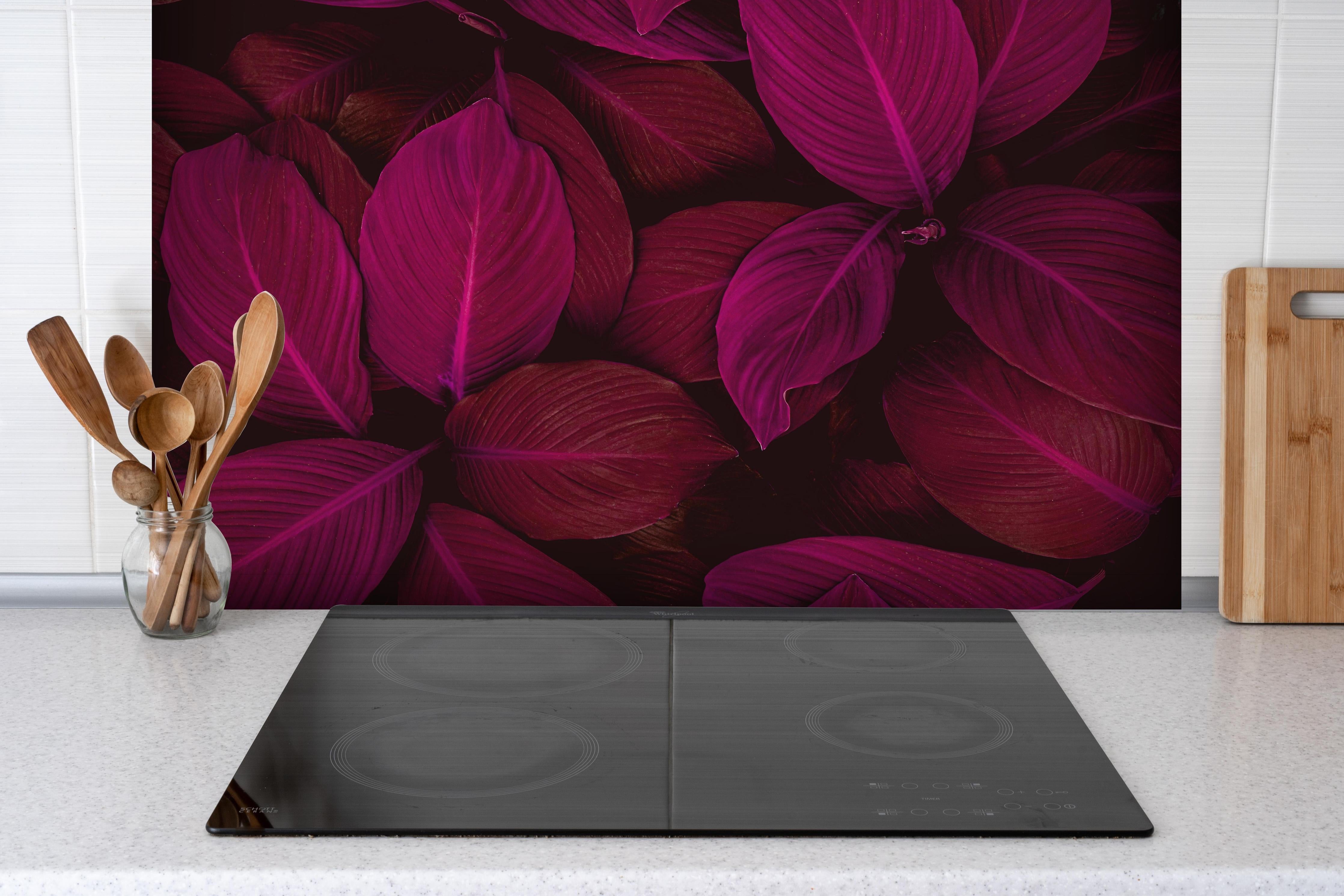 Spritzschutz - Farbenfrohe Spathiphyllum Blatttextur hinter einem Cerankochfeld zwischen Holz-Kochutensilien
