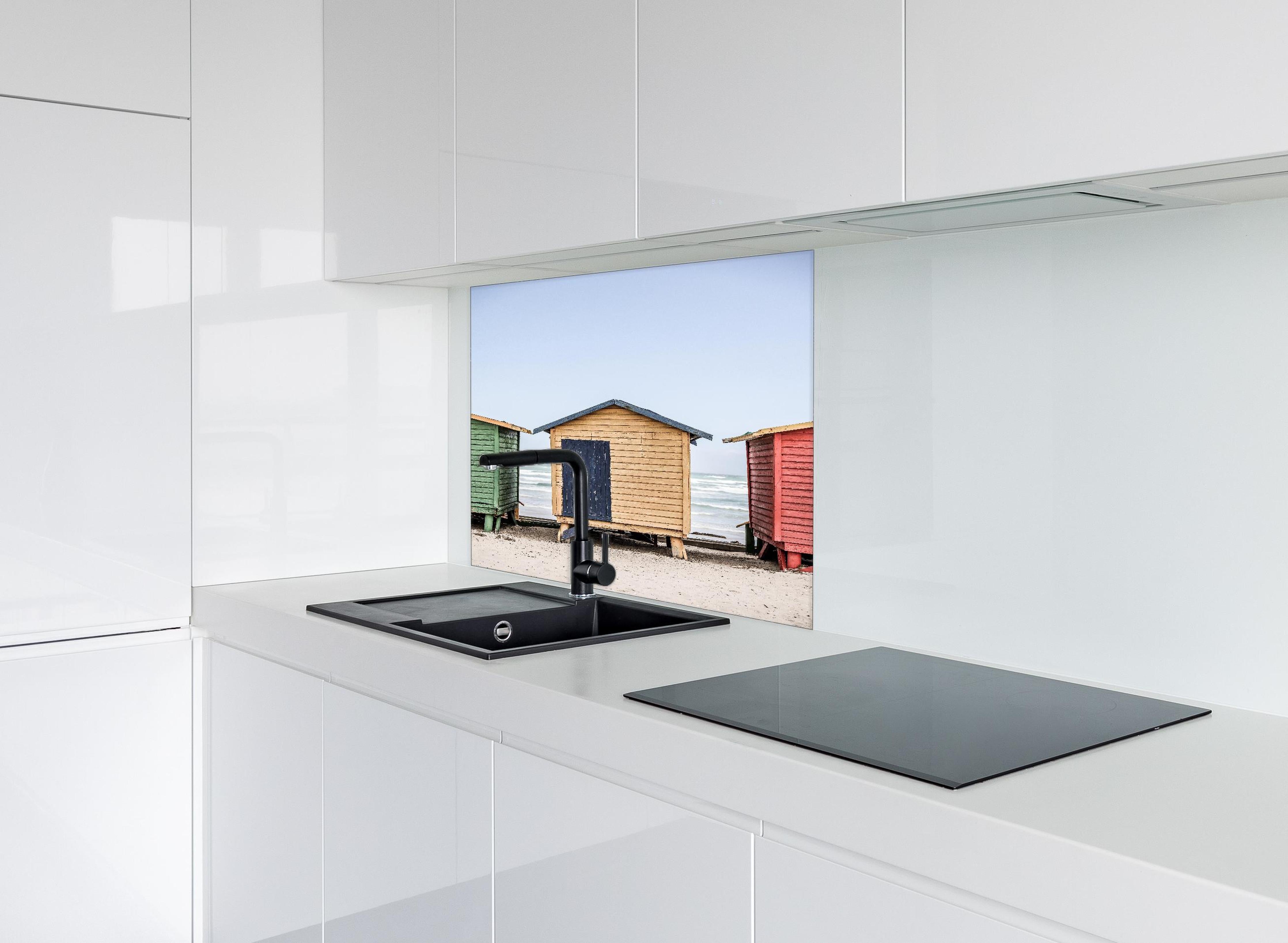 Spritzschutz - Farbenfrohe Strandhütten am Meeressand hinter einem Cerankochfeld zwischen Holz-Kochutensilien
