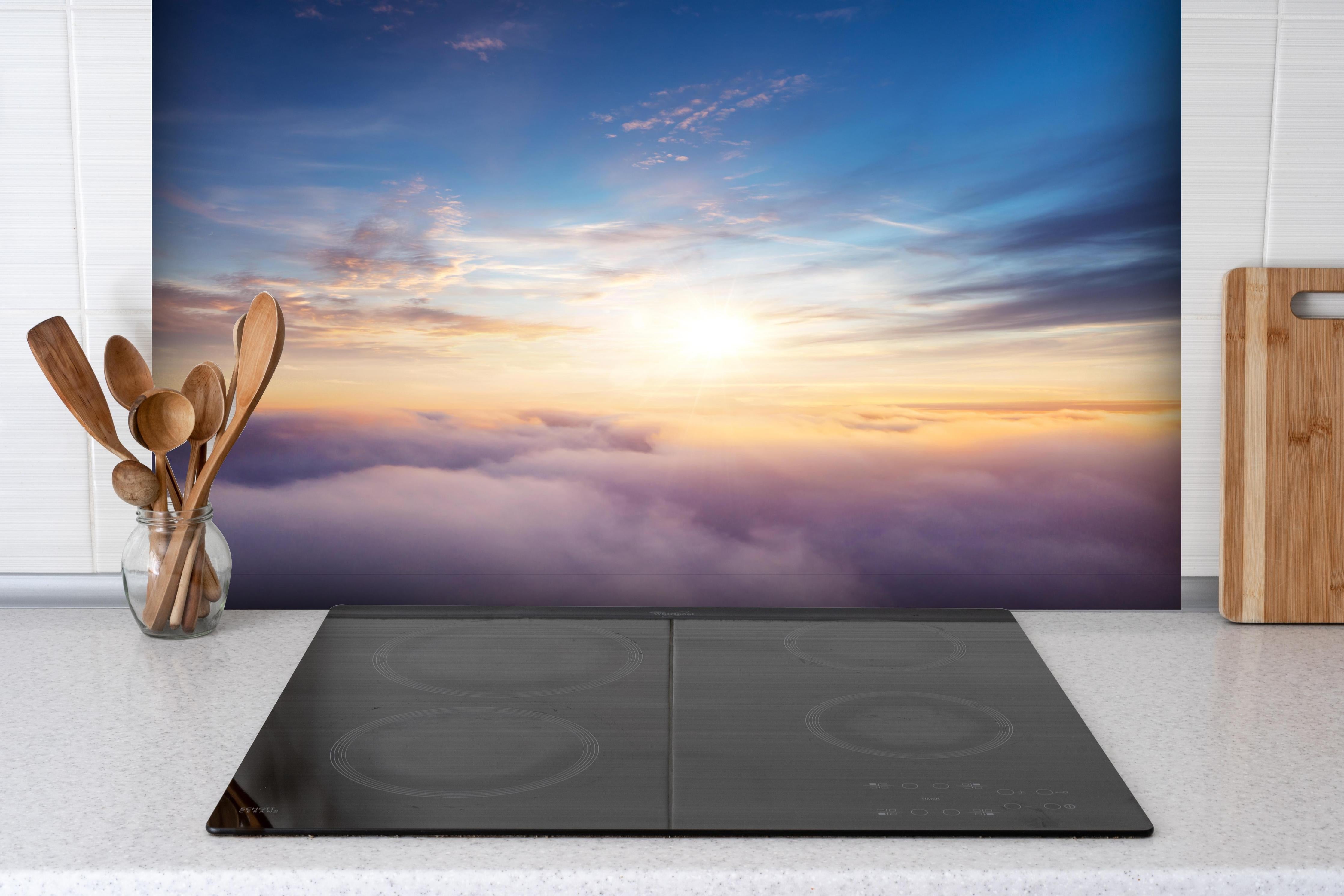 Spritzschutz - Farbenfrohe Wolken bei Sonnenaufgang hinter einem Cerankochfeld zwischen Holz-Kochutensilien
