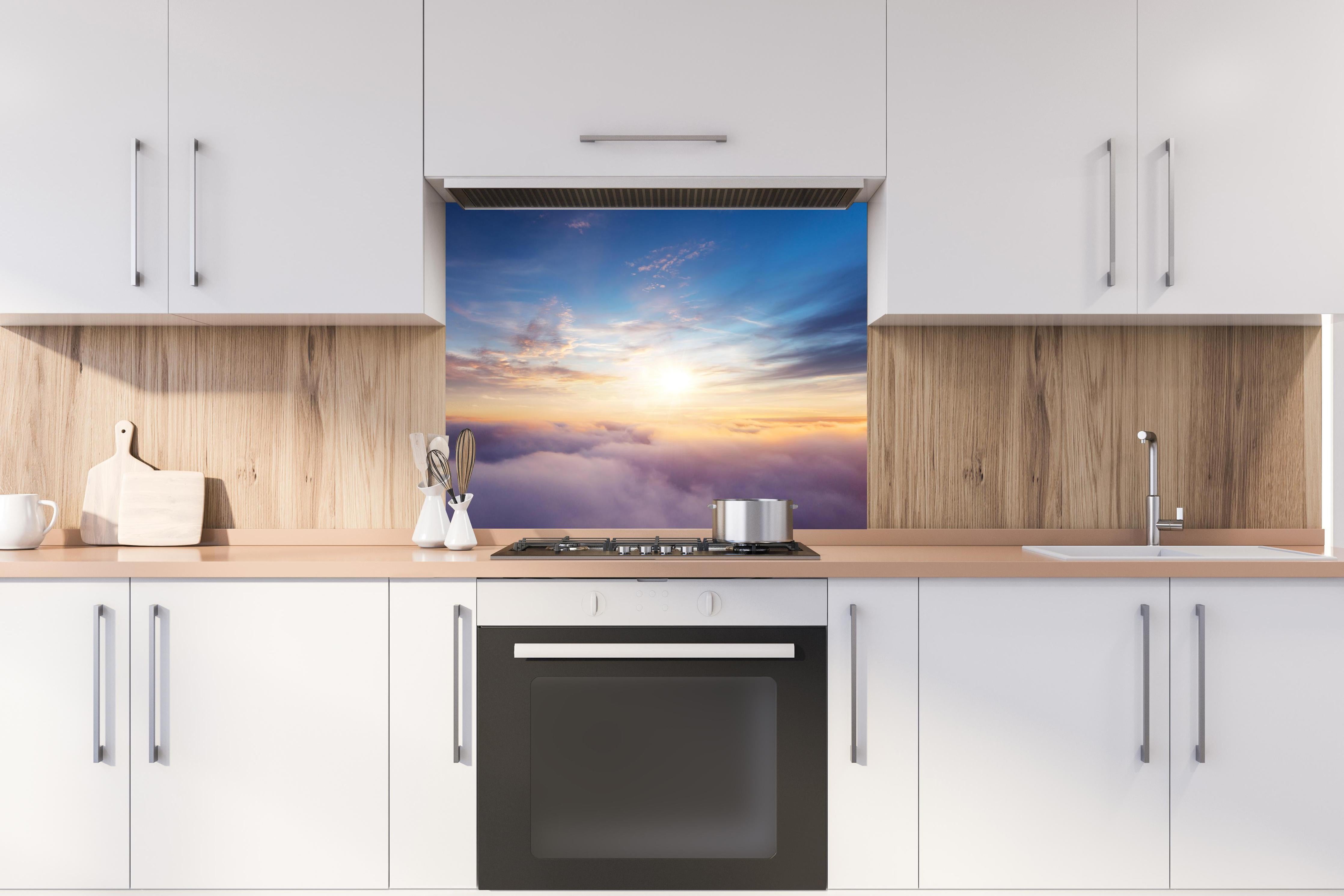 Spritzschutz - Farbenfrohe Wolken bei Sonnenaufgang hinter einem Cerankochfeld zwischen Holz-Kochutensilien
