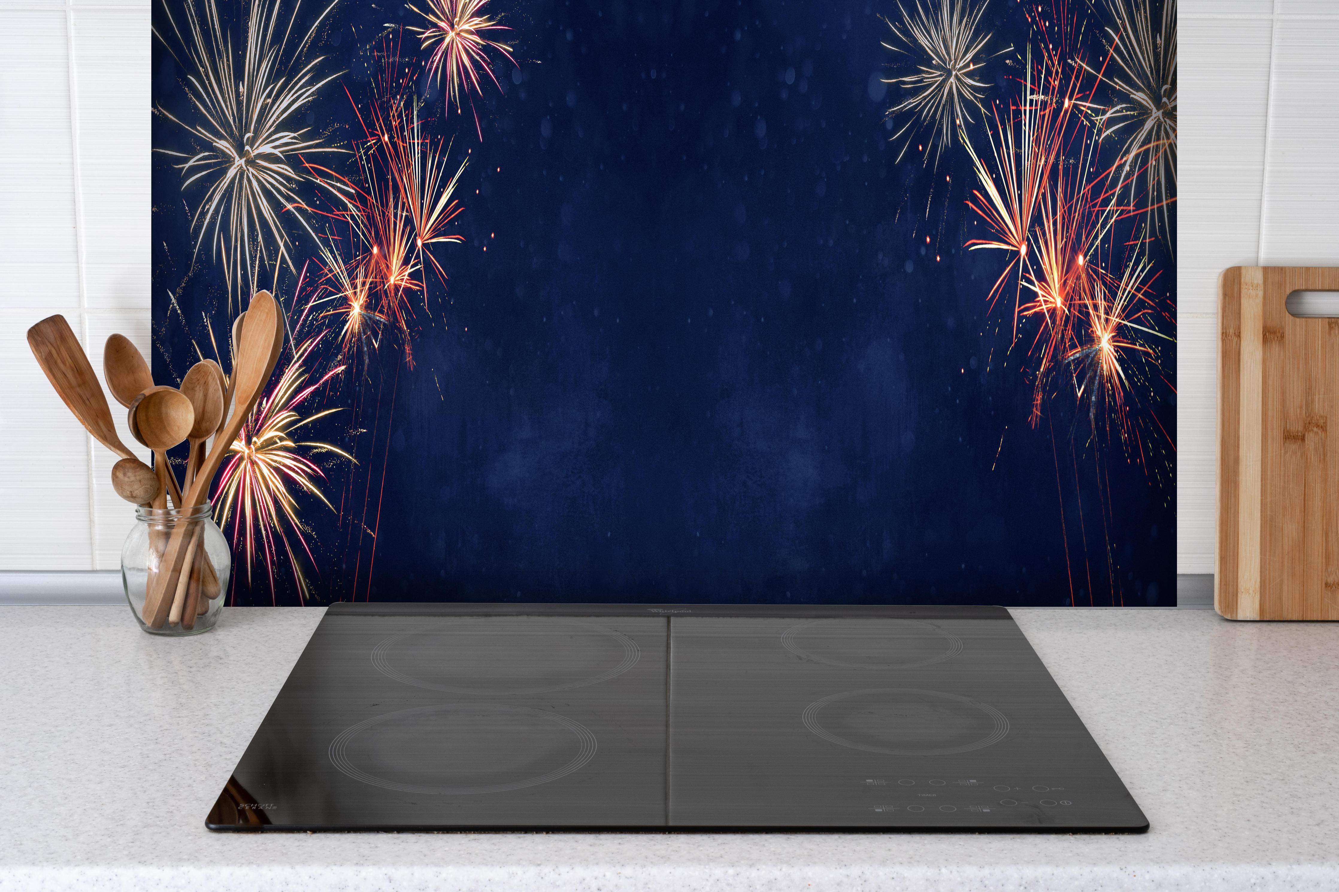 Spritzschutz - Farbenfrohes Feuerwerk zu Neujahr 2023 hinter einem Cerankochfeld zwischen Holz-Kochutensilien
