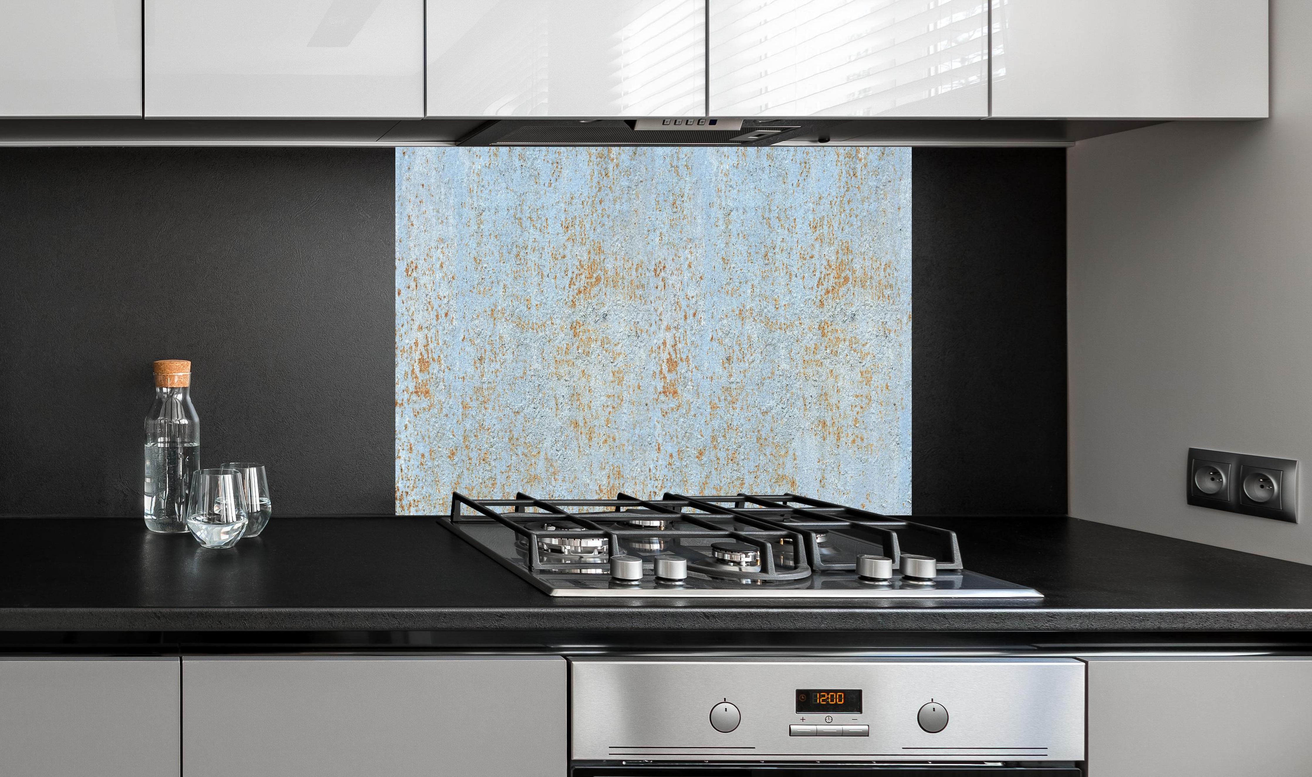 Spritzschutz - Farbflocken auf rostigem Metallblech hinter einem Cerankochfeld zwischen Holz-Kochutensilien
