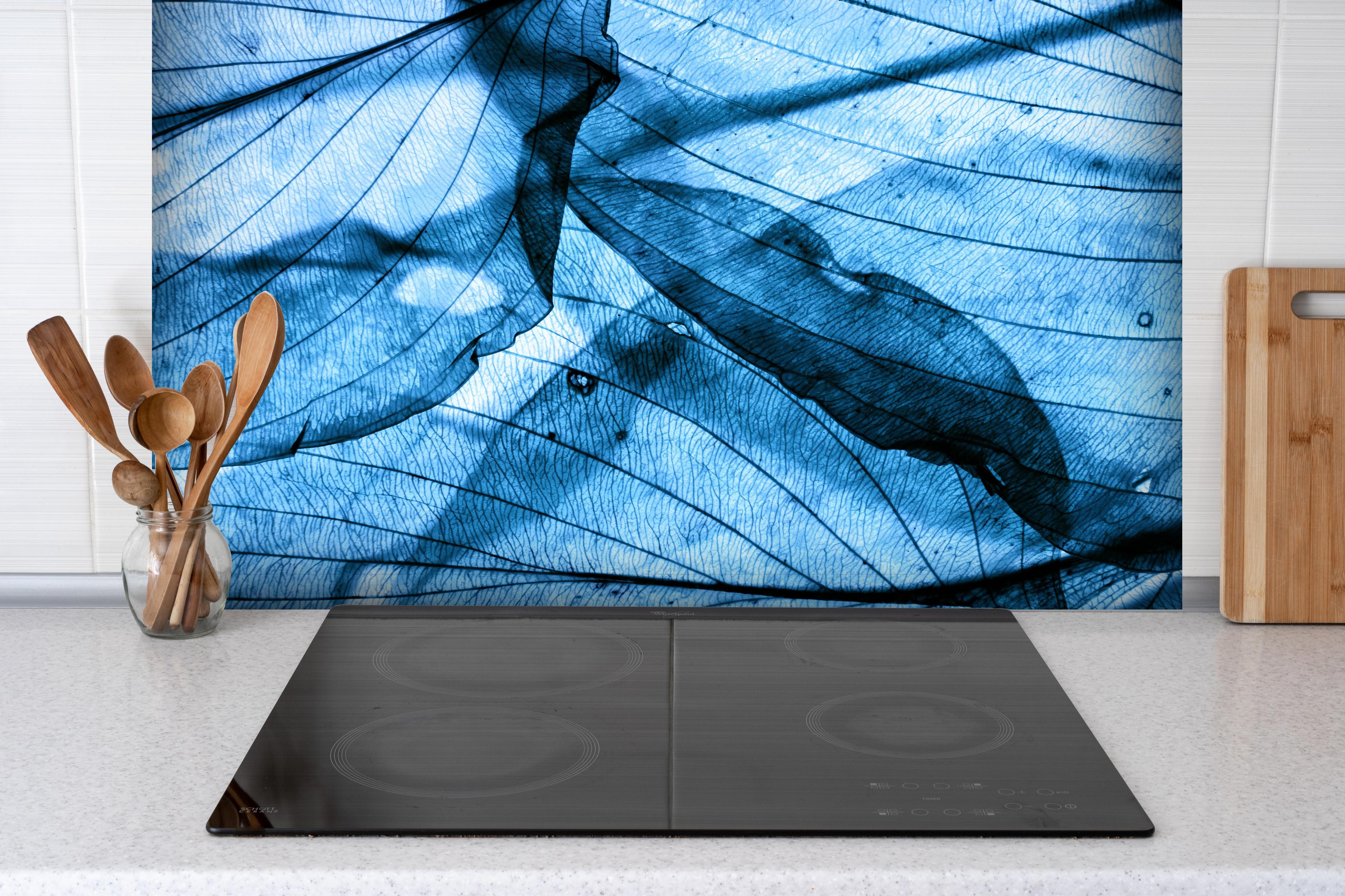Spritzschutz - Feine Herbstblatt-Struktur in Blautönen hinter einem Cerankochfeld zwischen Holz-Kochutensilien
