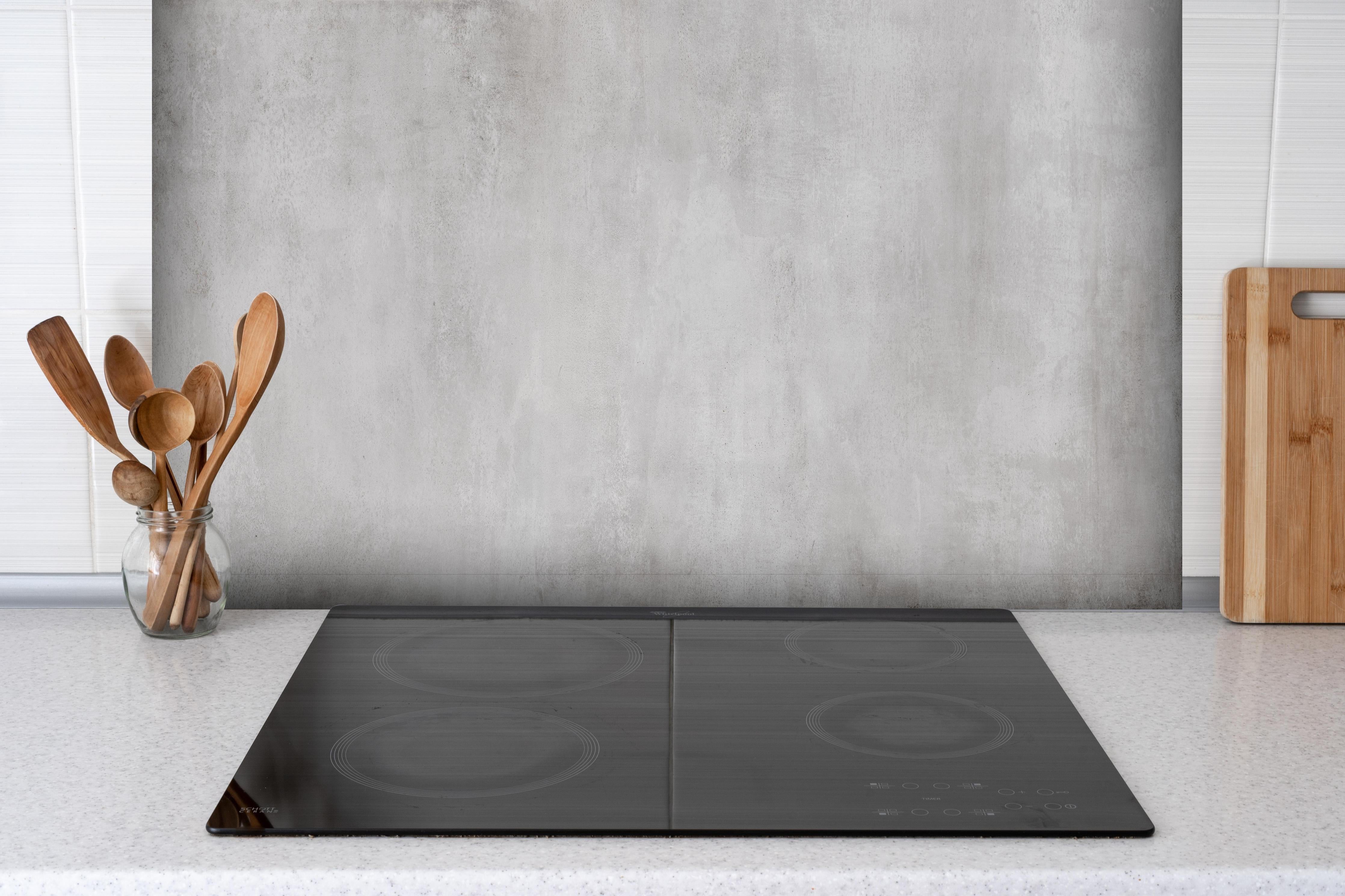 Spritzschutz - Feine Zement- Struktur hinter einem Cerankochfeld zwischen Holz-Kochutensilien
