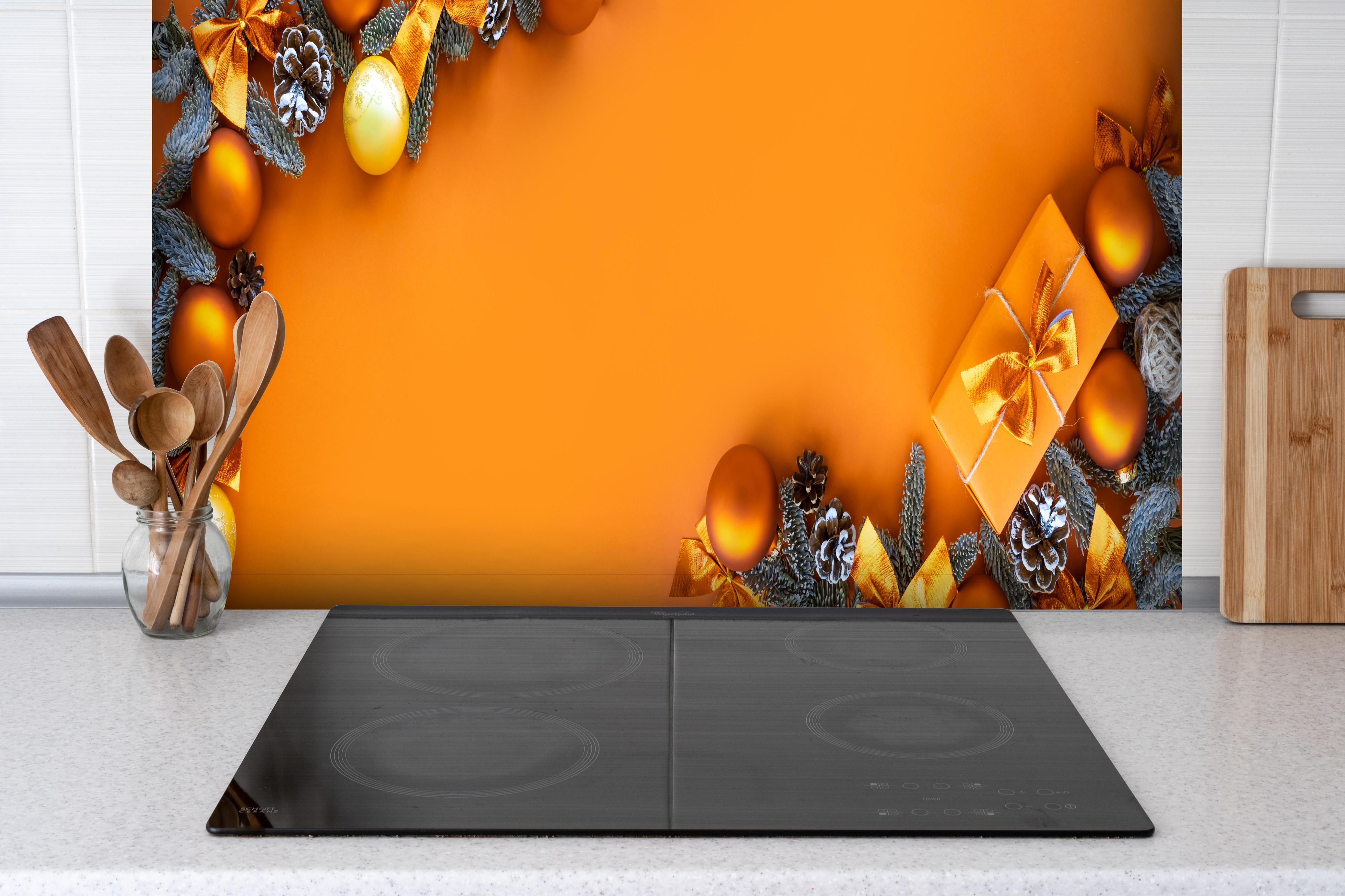 Spritzschutz - Festliches Weihnachtsdekor mit goldenen Akzenten hinter einem Cerankochfeld zwischen Holz-Kochutensilien
