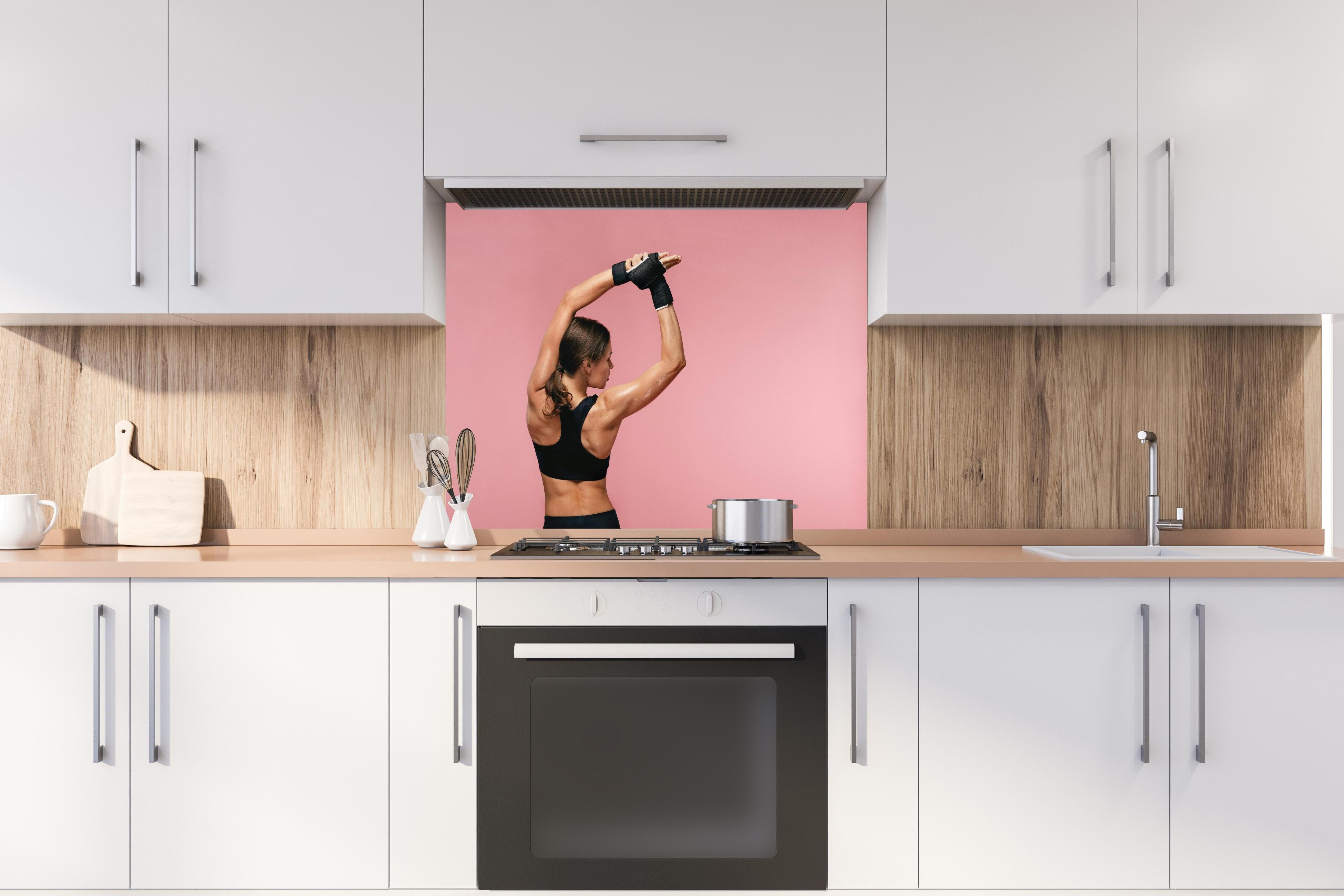 Spritzschutz - Fitness Frau streckt sich vor Training hinter einem Cerankochfeld zwischen Holz-Kochutensilien
