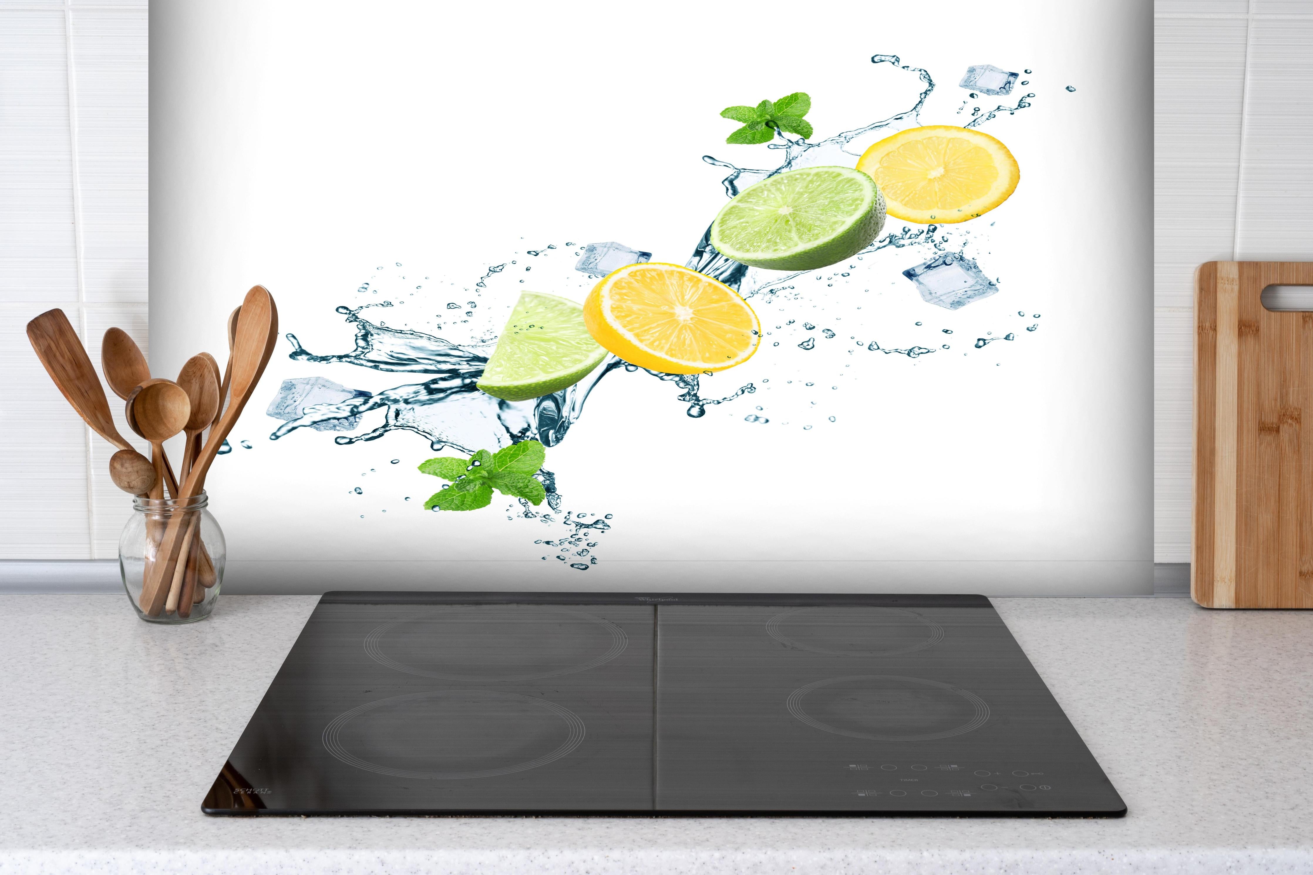 Spritzschutz - Frische Zitrusfrüchte und Eiswürfel Splash hinter einem Cerankochfeld zwischen Holz-Kochutensilien

