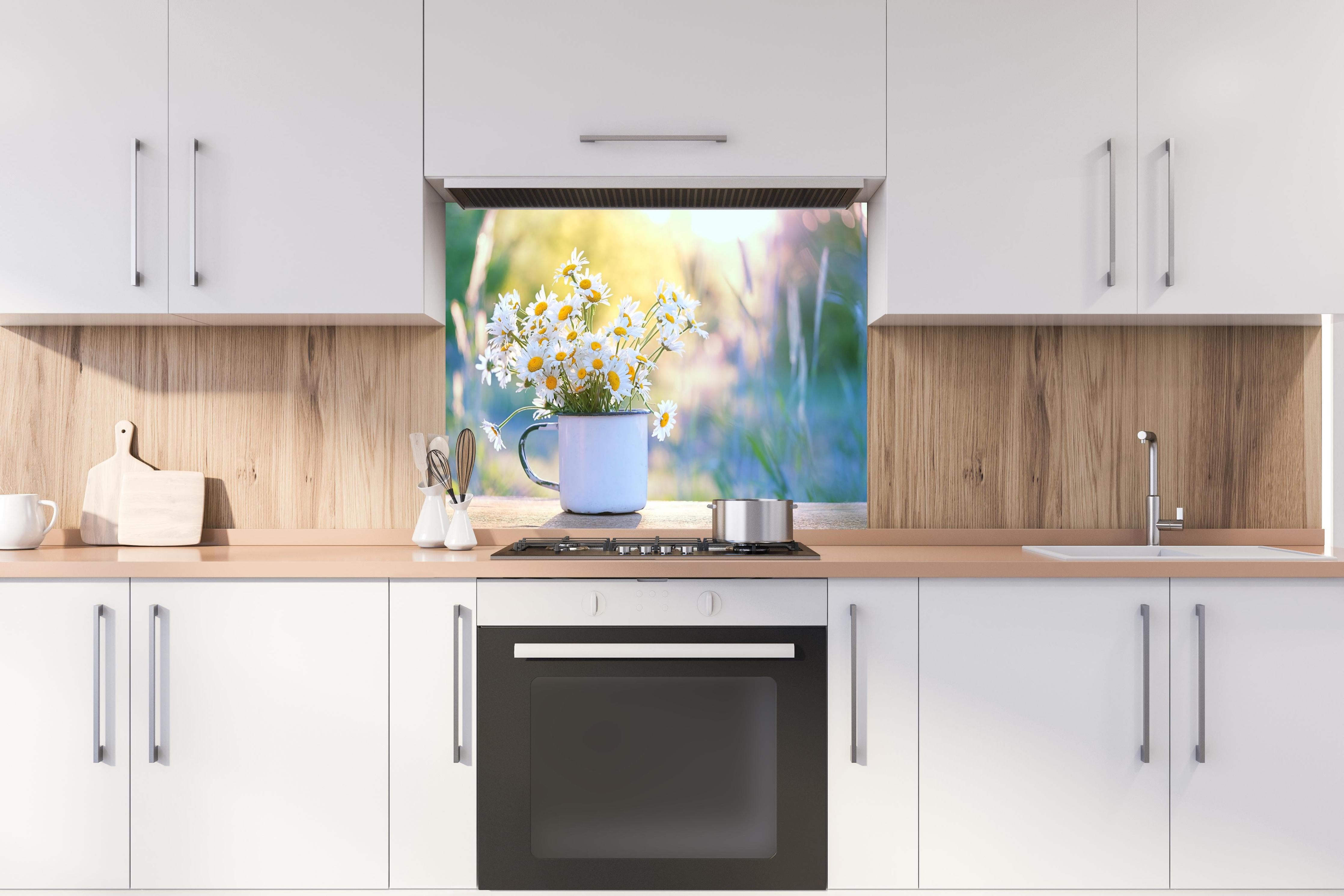 Spritzschutz - Gänseblümchen im Licht des Sonnenuntergangs hinter einem Cerankochfeld zwischen Holz-Kochutensilien
