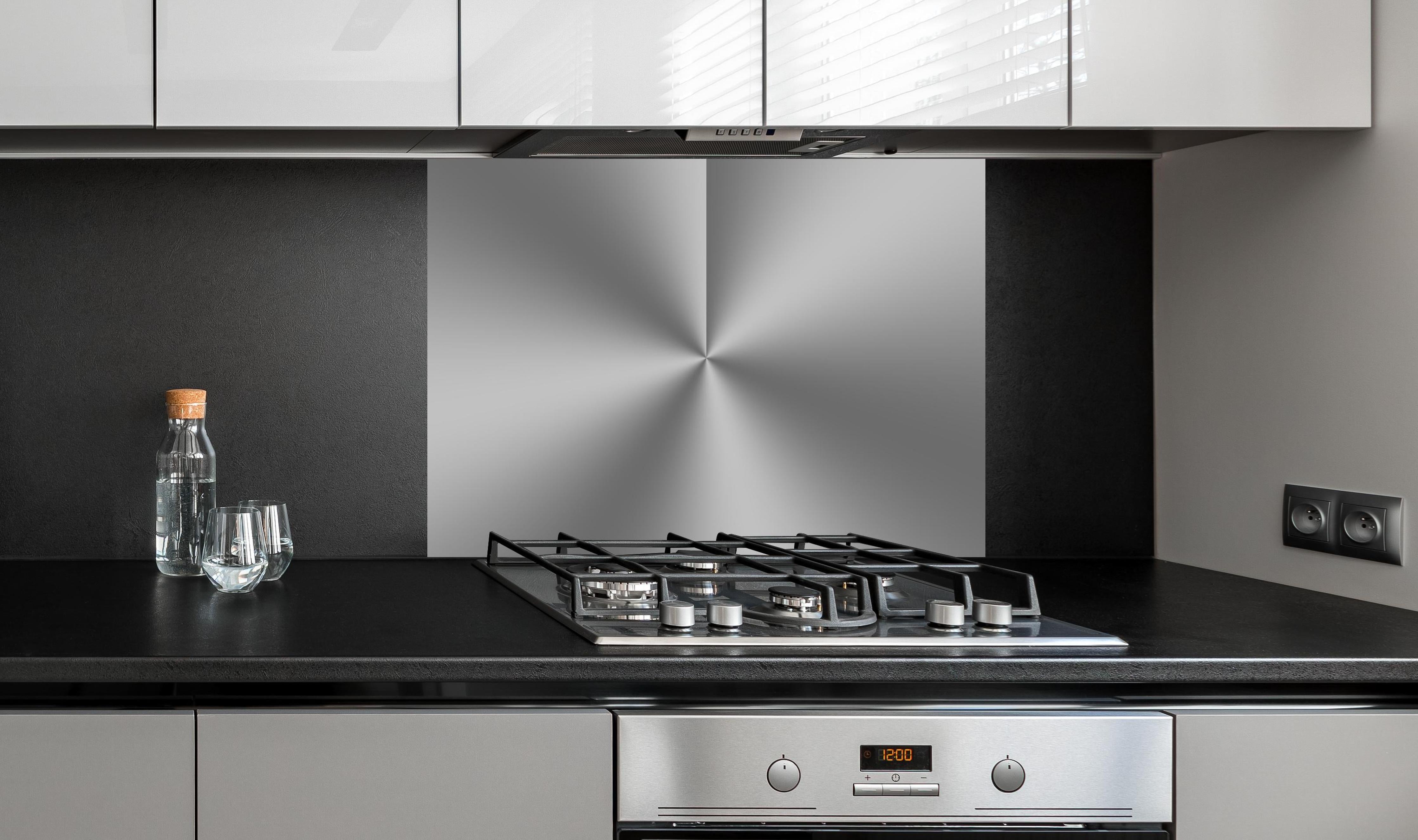 Spritzschutz - Gebürstetes Metall hinter einem Cerankochfeld zwischen Holz-Kochutensilien
