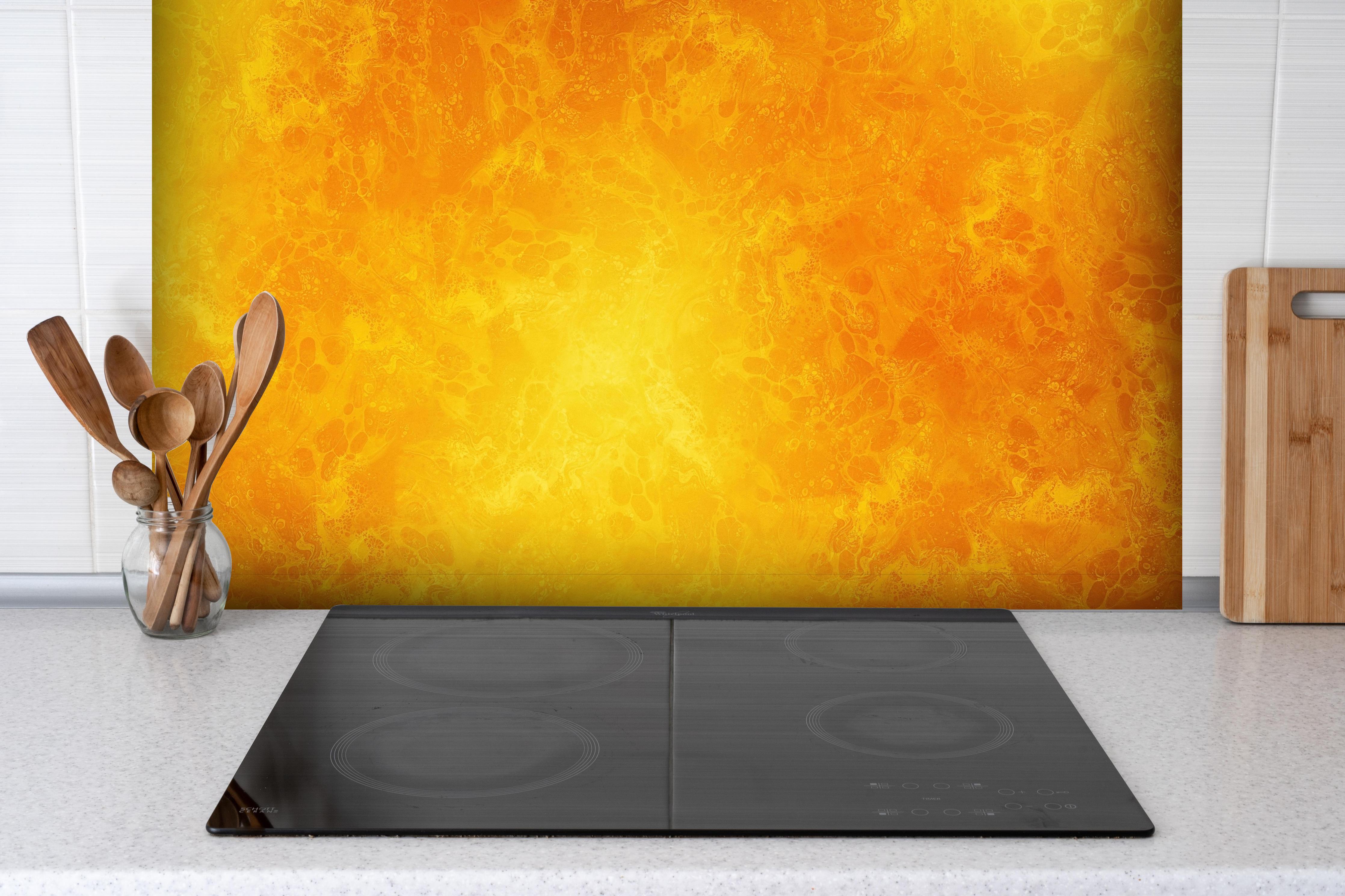 Spritzschutz - Gelbes Farbmuster hinter einem Cerankochfeld zwischen Holz-Kochutensilien
