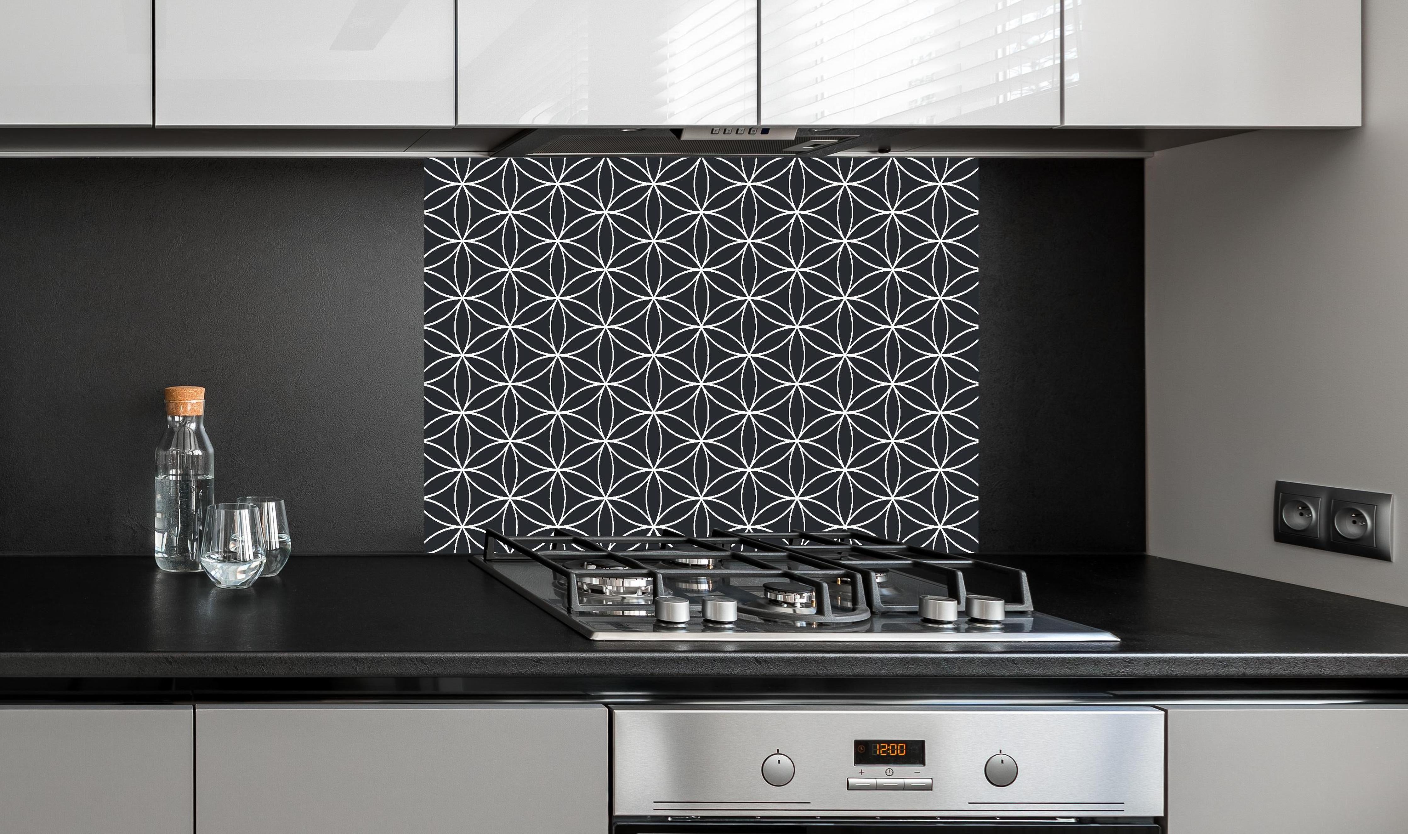 Spritzschutz - Geometrica Fiori Carbone hinter einem Cerankochfeld zwischen Holz-Kochutensilien
