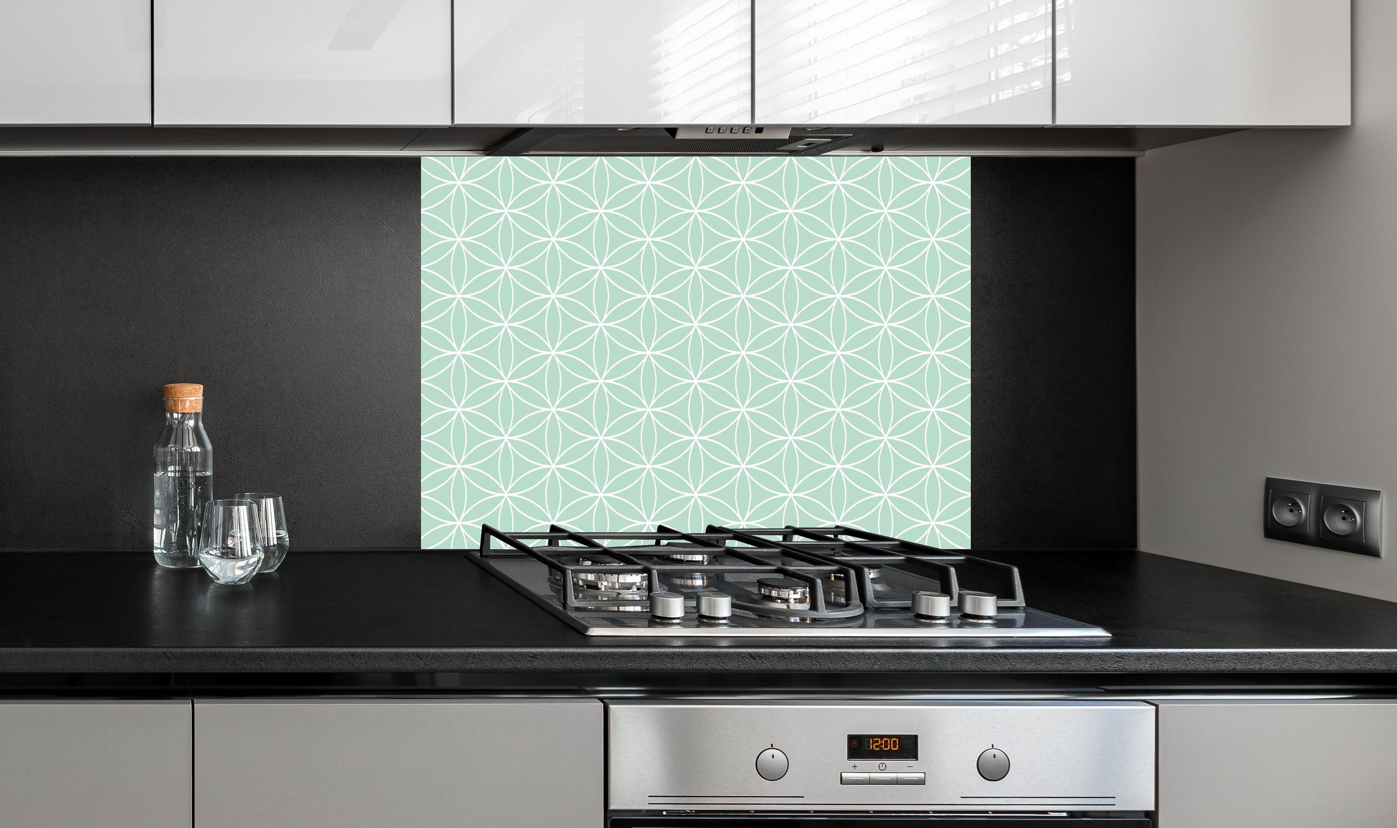 Spritzschutz - Geometrica Fiori Menta hinter einem Cerankochfeld zwischen Holz-Kochutensilien
