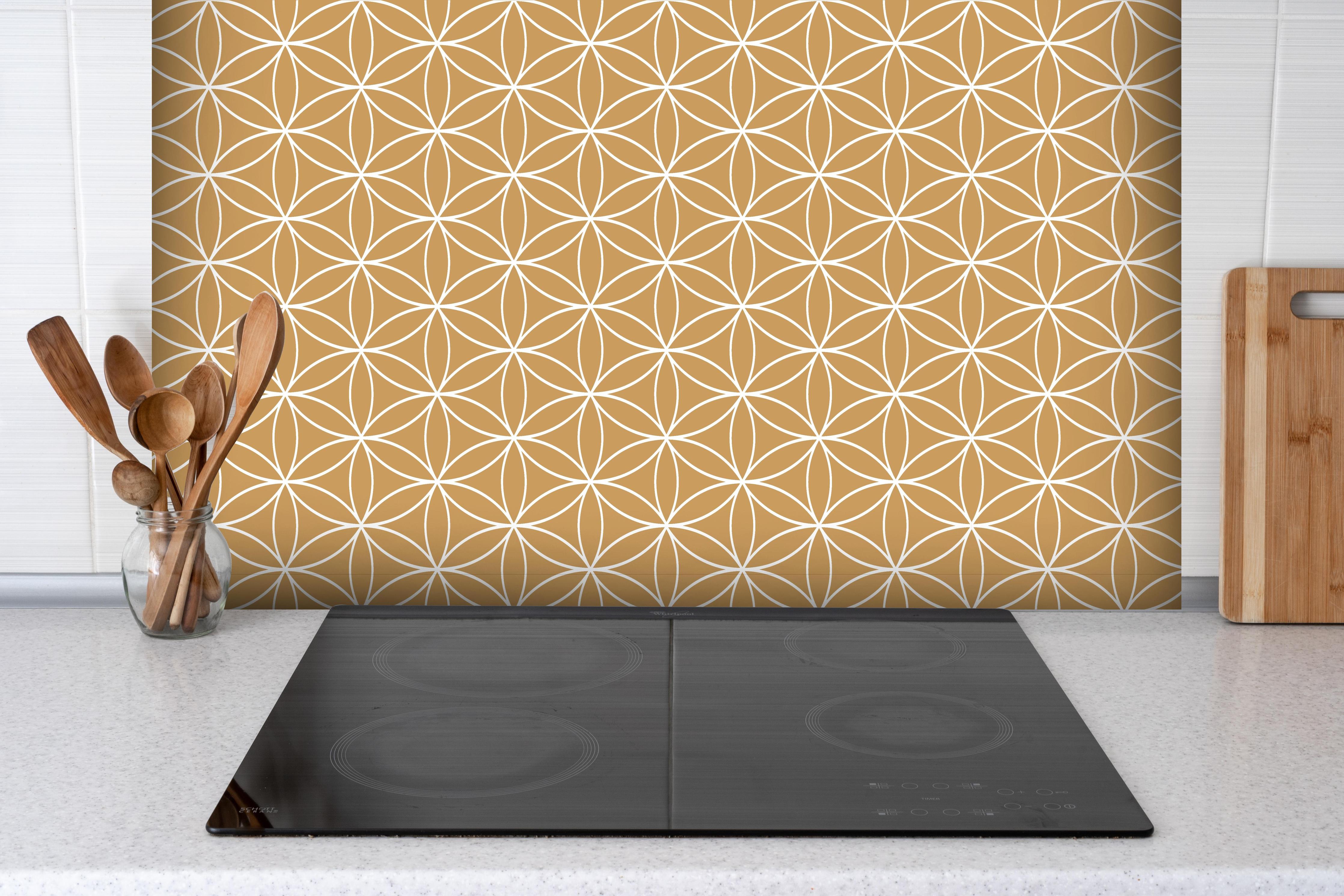 Spritzschutz - Geometrica Fiori Ocra hinter einem Cerankochfeld zwischen Holz-Kochutensilien
