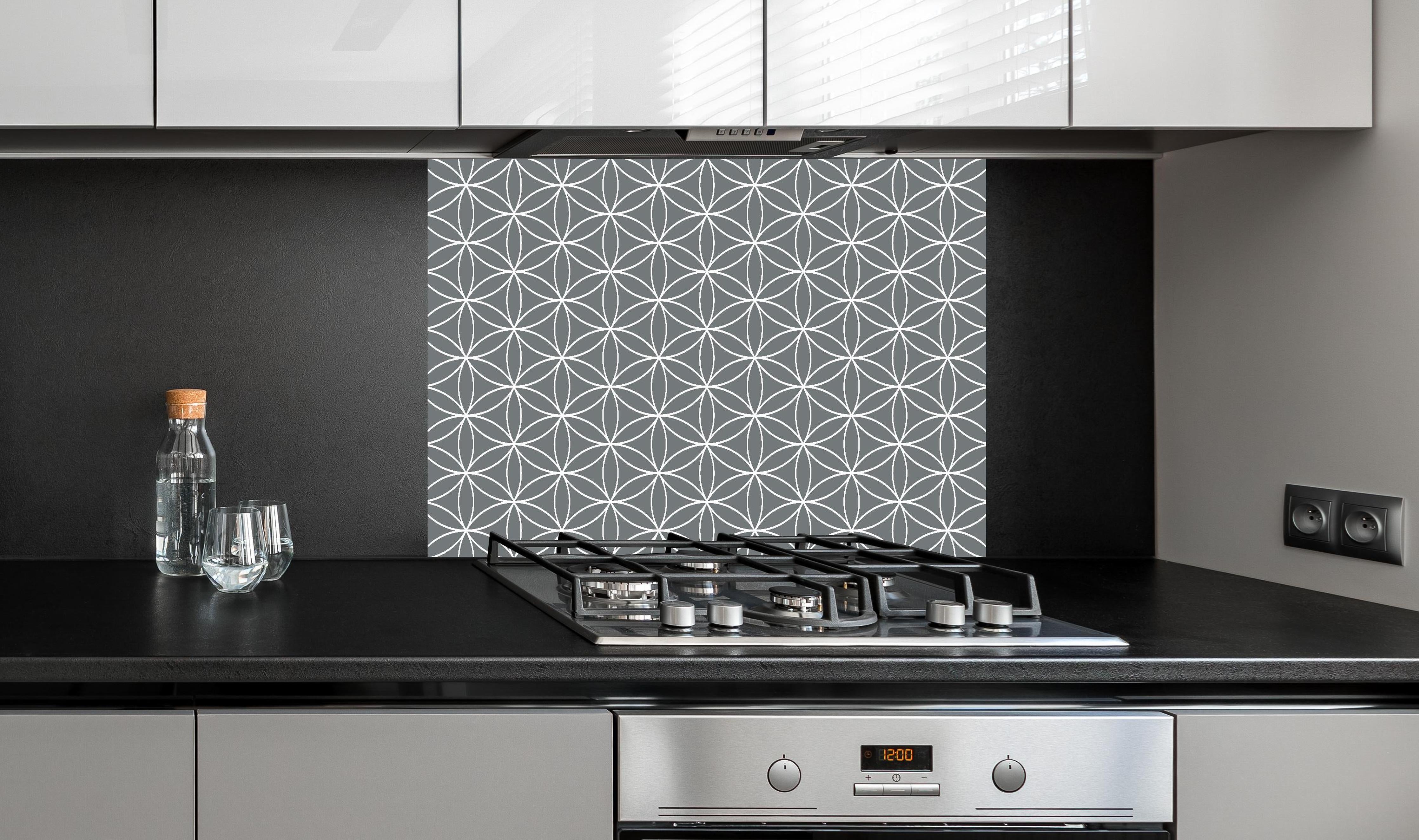 Spritzschutz - Geometrica Fiori Piombo hinter einem Cerankochfeld zwischen Holz-Kochutensilien

