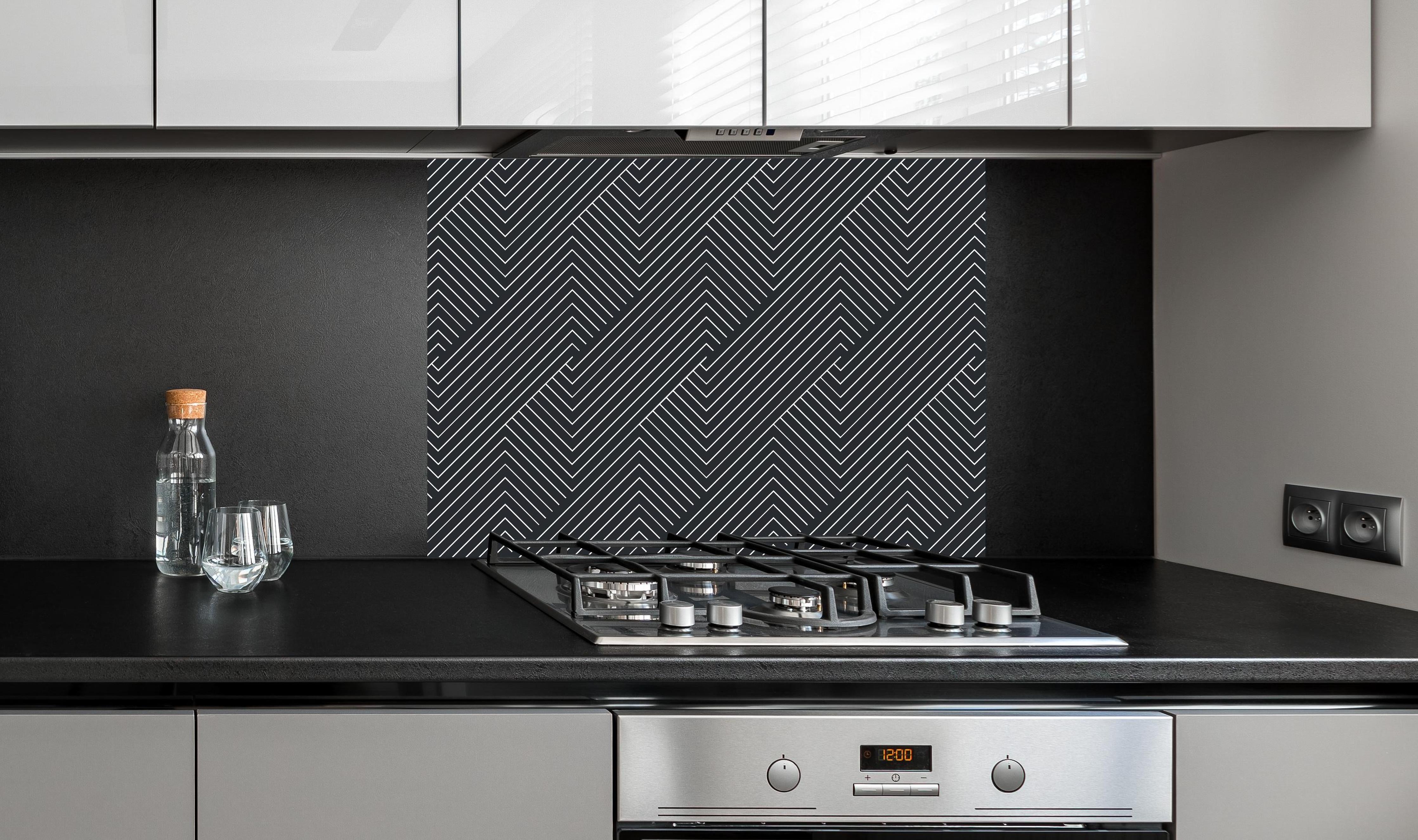 Spritzschutz - Geometrica Intreccio Carbone hinter einem Cerankochfeld zwischen Holz-Kochutensilien
